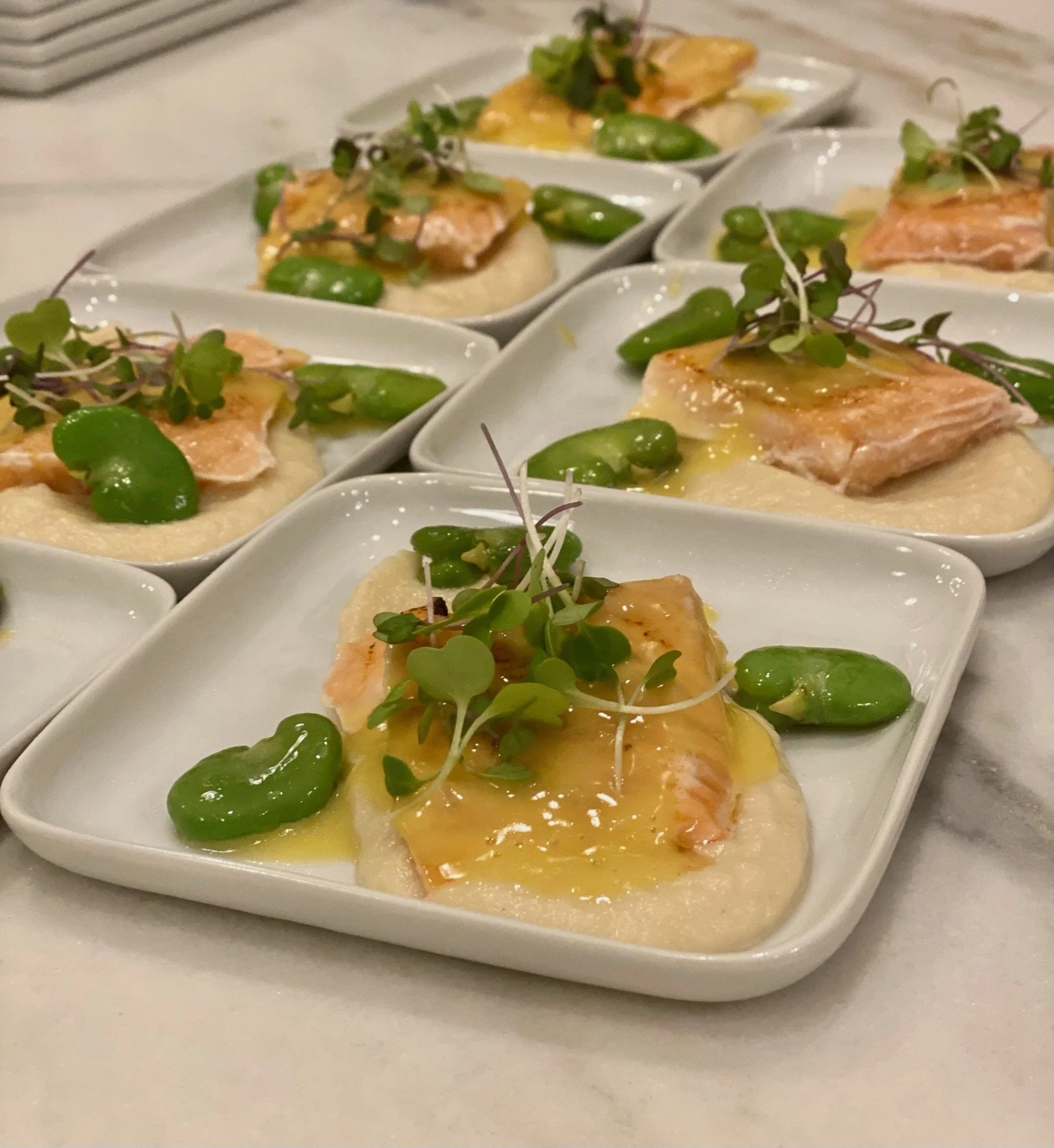 Fish appetizer on a square plate with fava beans.