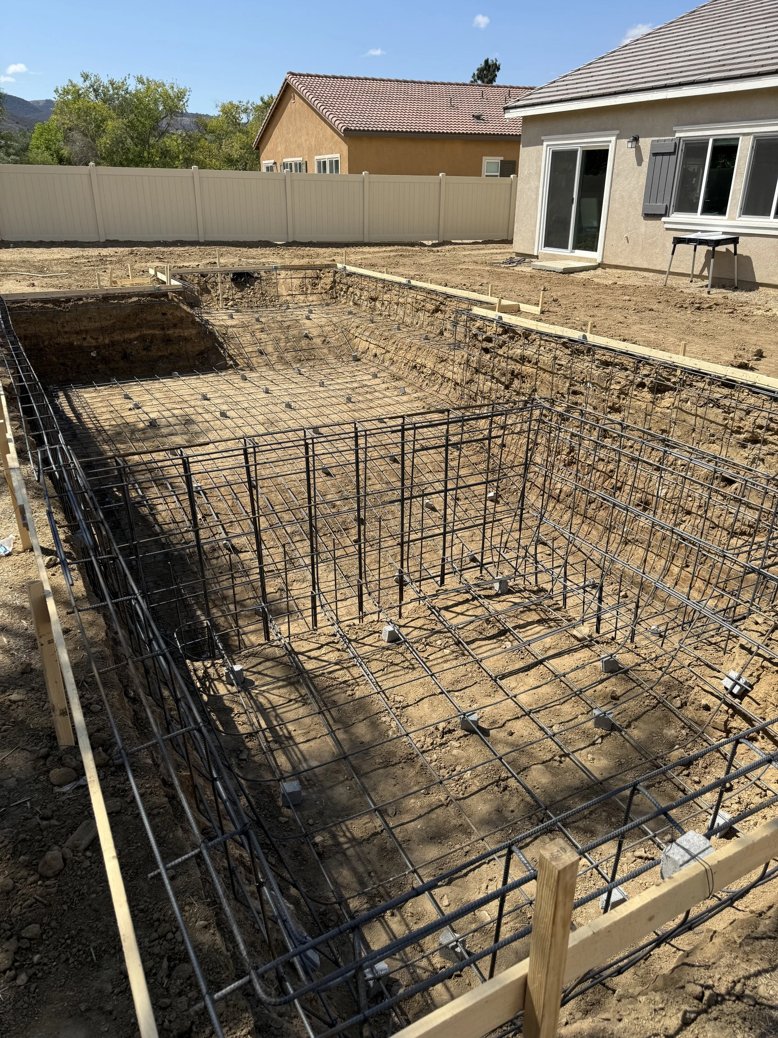 Construction site with reinforced steel rebar framework in an excavation site for building foundation in a residential backyard.