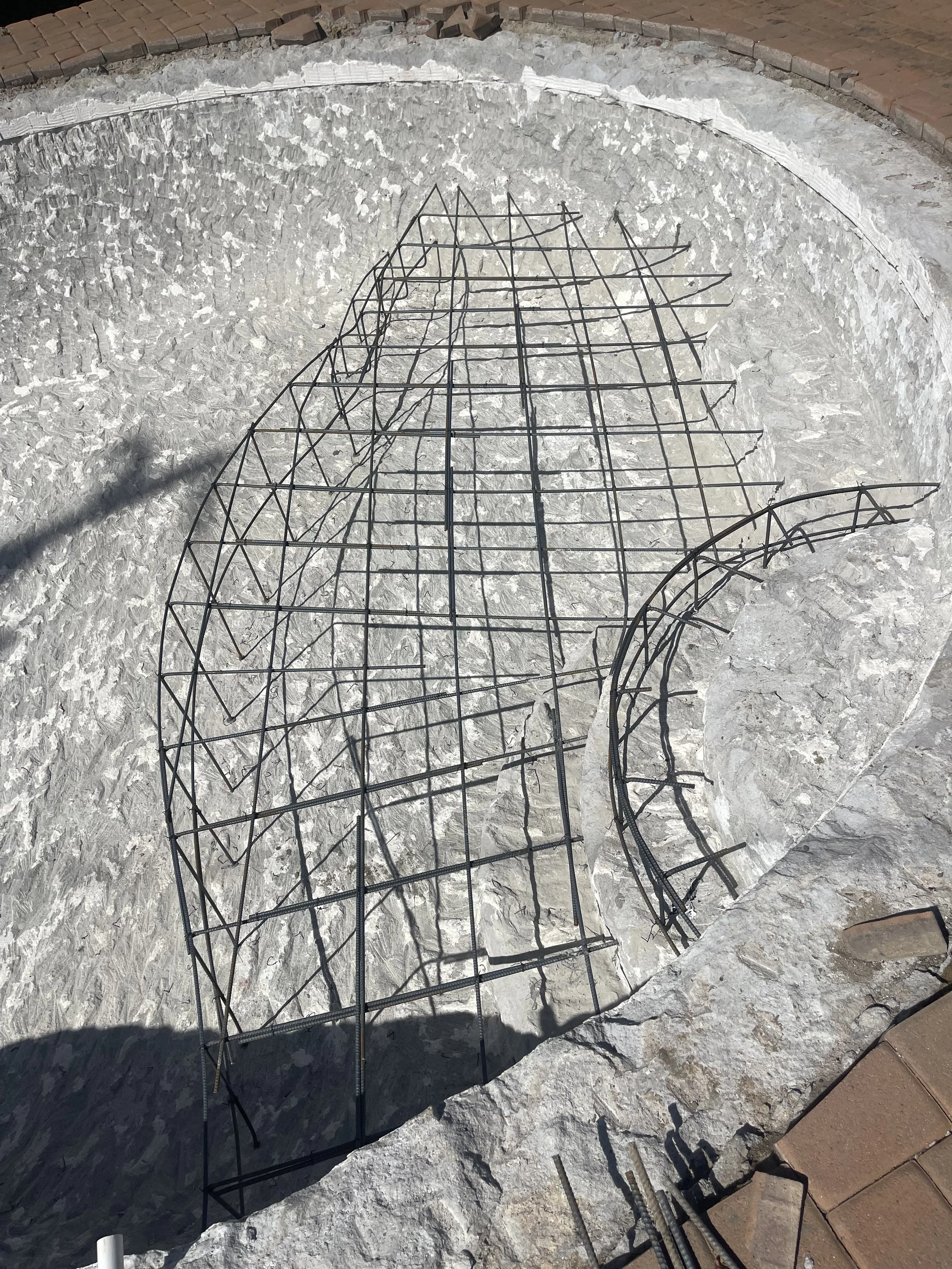 An unfinished circular stone fire pit with metal rebar for reinforcement, surrounded by a brick patio.