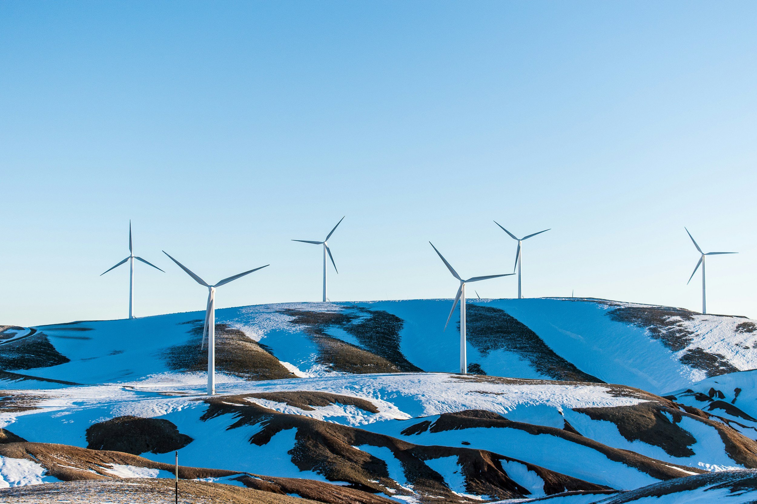 Wind turbines on snowy hills under a clear blue sky.