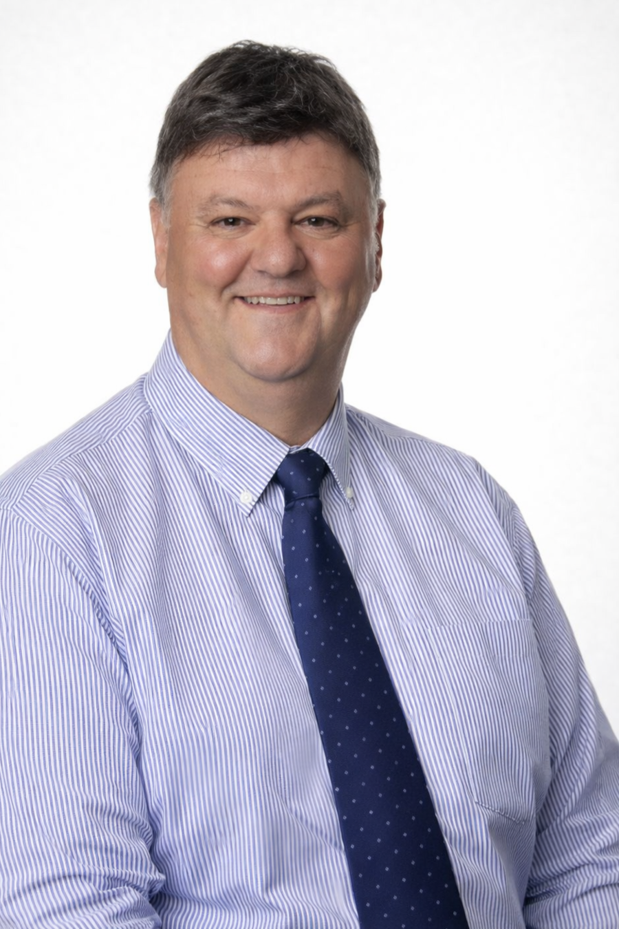 Smiling middle-aged man with short dark hair wearing a blue and white striped dress shirt and a dark tie, posing against a white background.