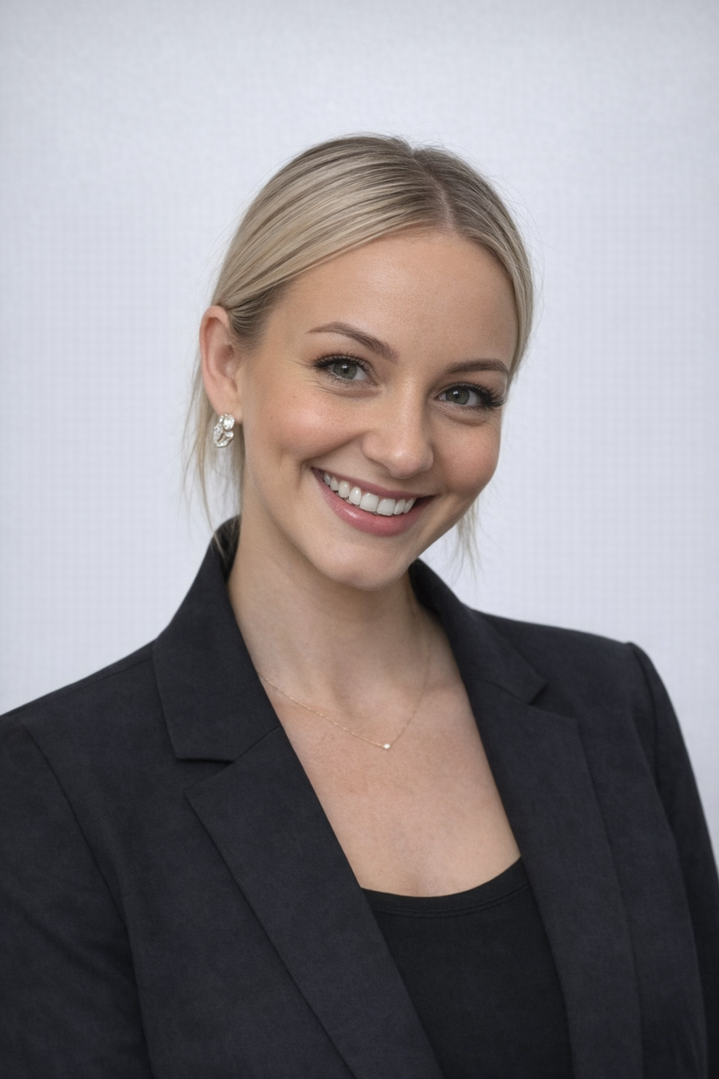 A smiling young woman with blonde hair, wearing sunglasses on her head and earrings.