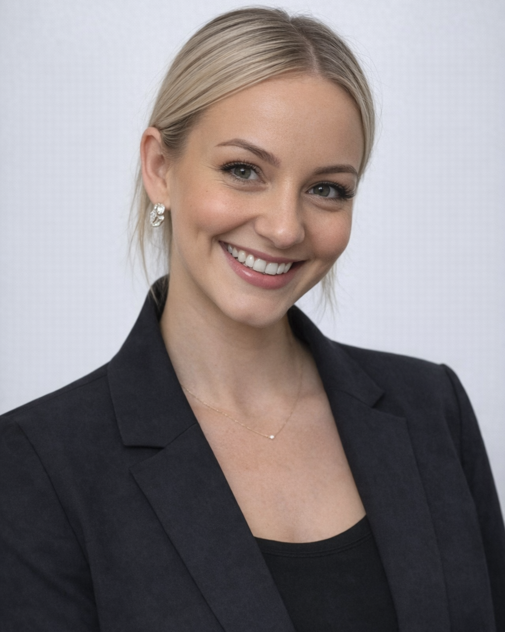 A smiling young woman with blonde hair, wearing sunglasses on her head and earrings.