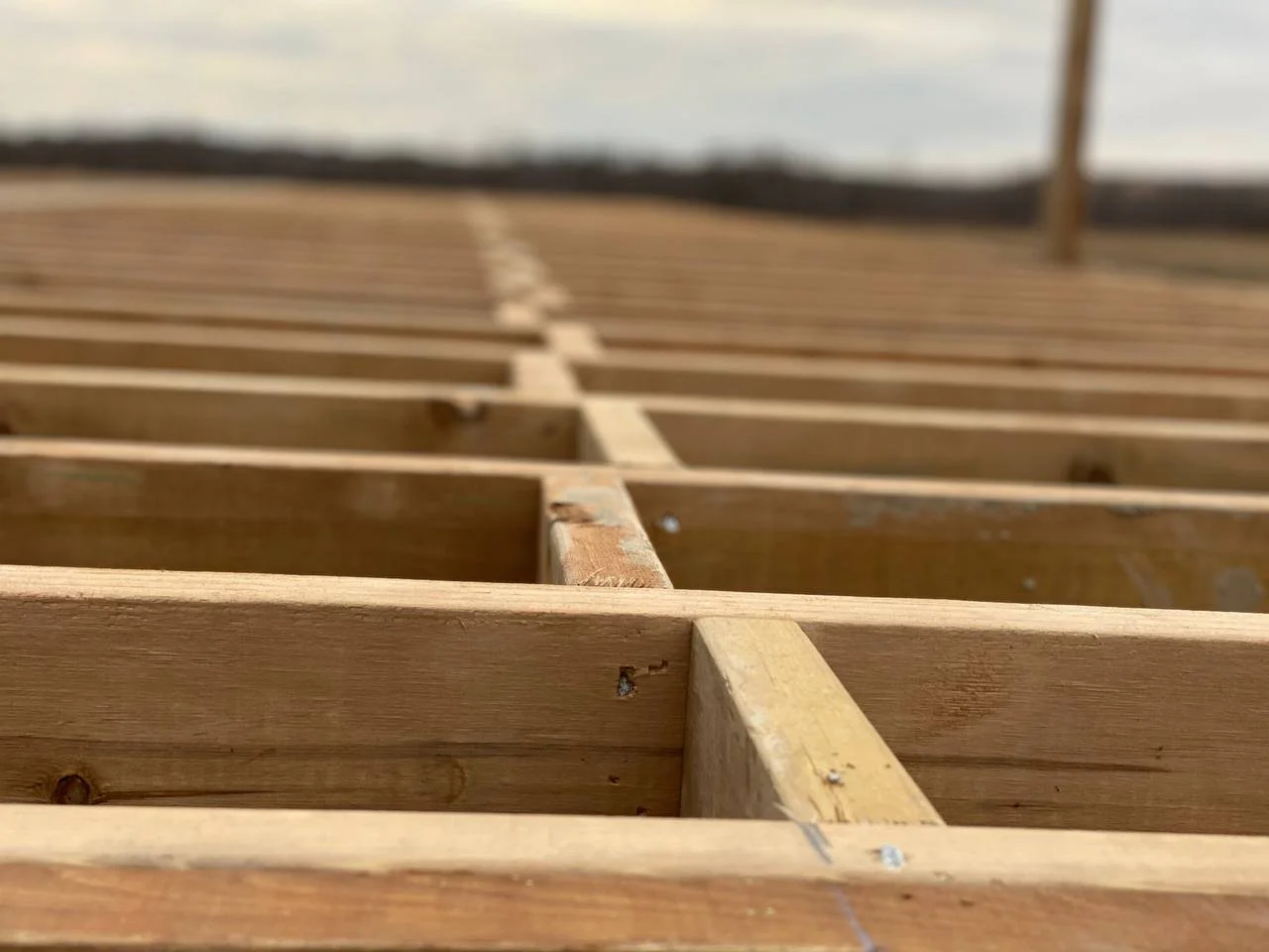 Close-up of a wooden dock structure with horizontal and vertical beams, leading out towards the water and horizon in the distance.