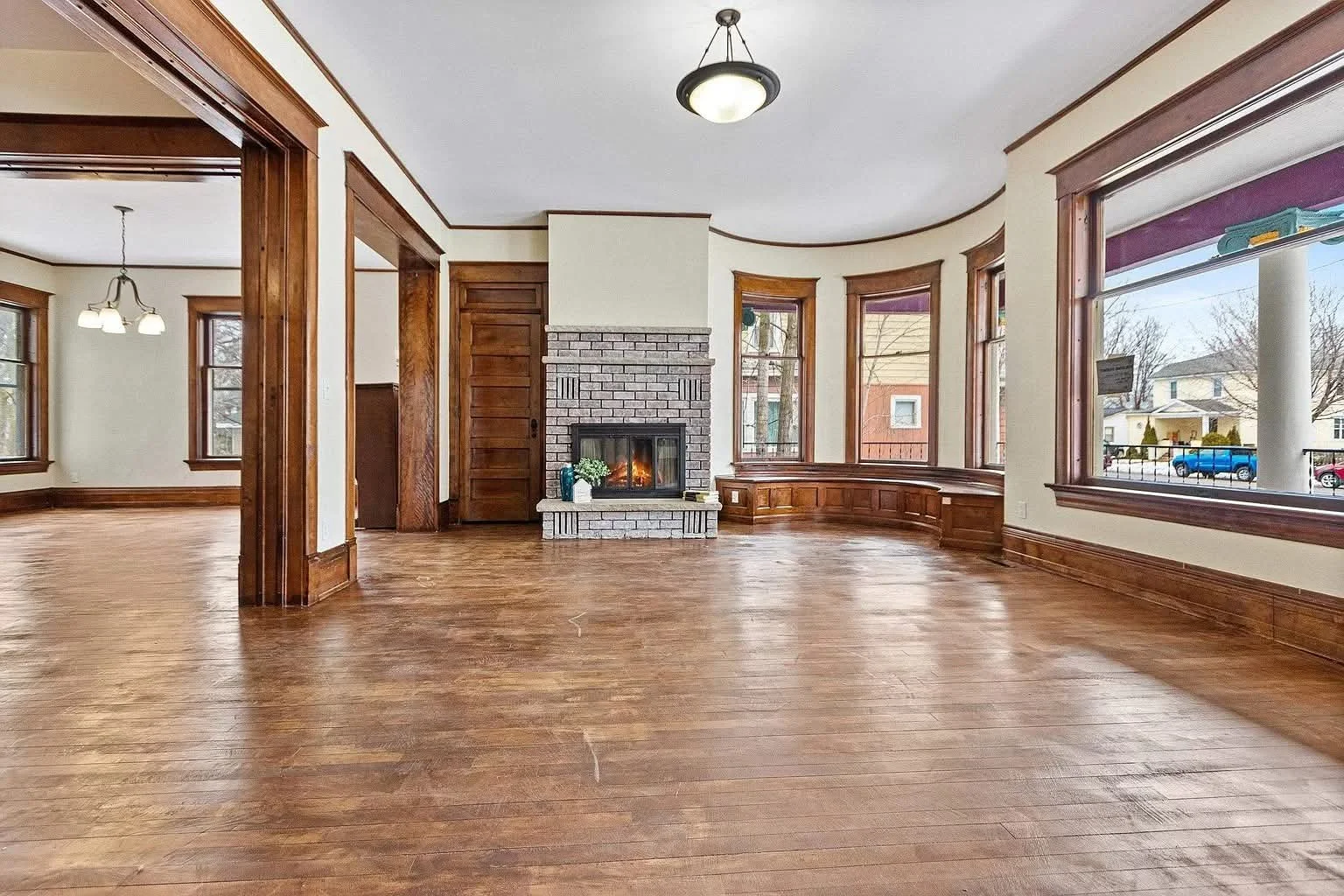 A large Victorian-style house with a wraparound porch, illuminated from inside, at dusk. The house has multiple stories, a turret, and decorative trim, with the sky dark blue in the background.