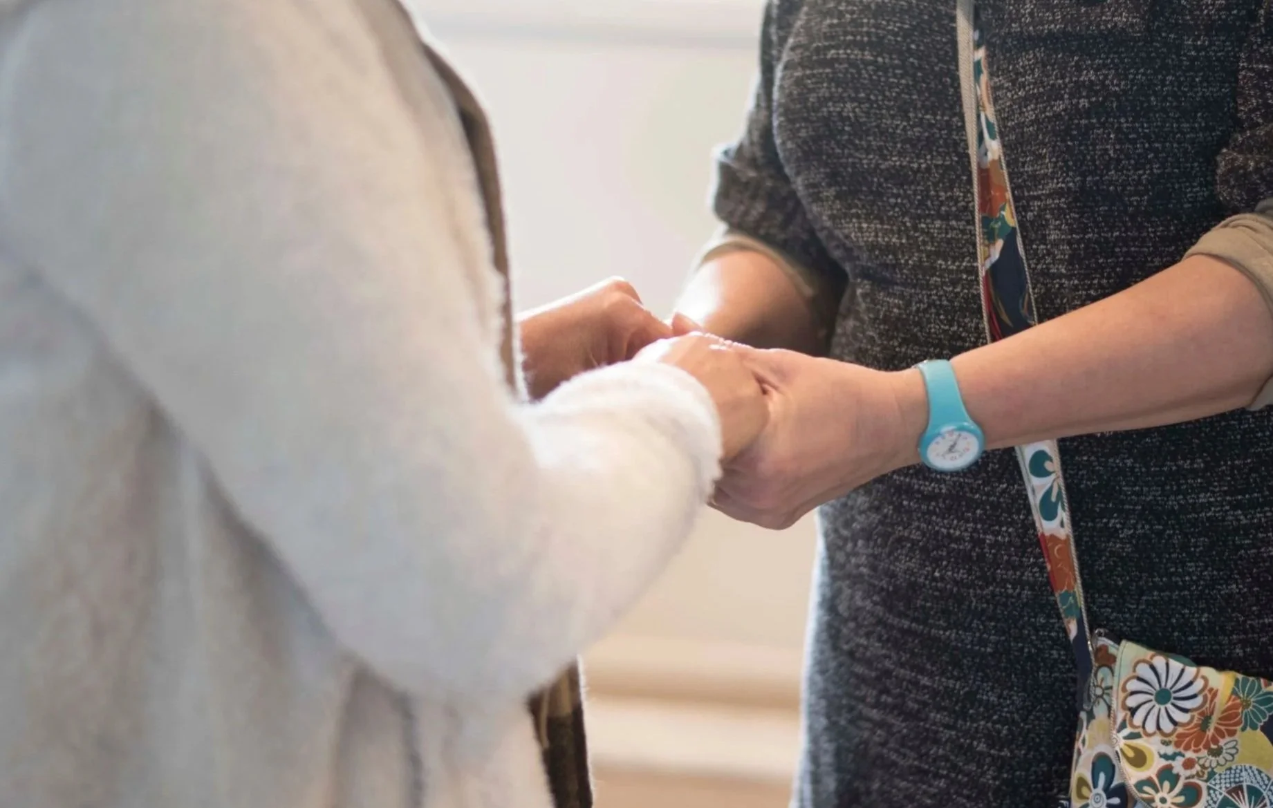 Two people holding hands, one wearing a white sweater and the other wearing a dark patterned top and a colorful lanyard, in an embrace.