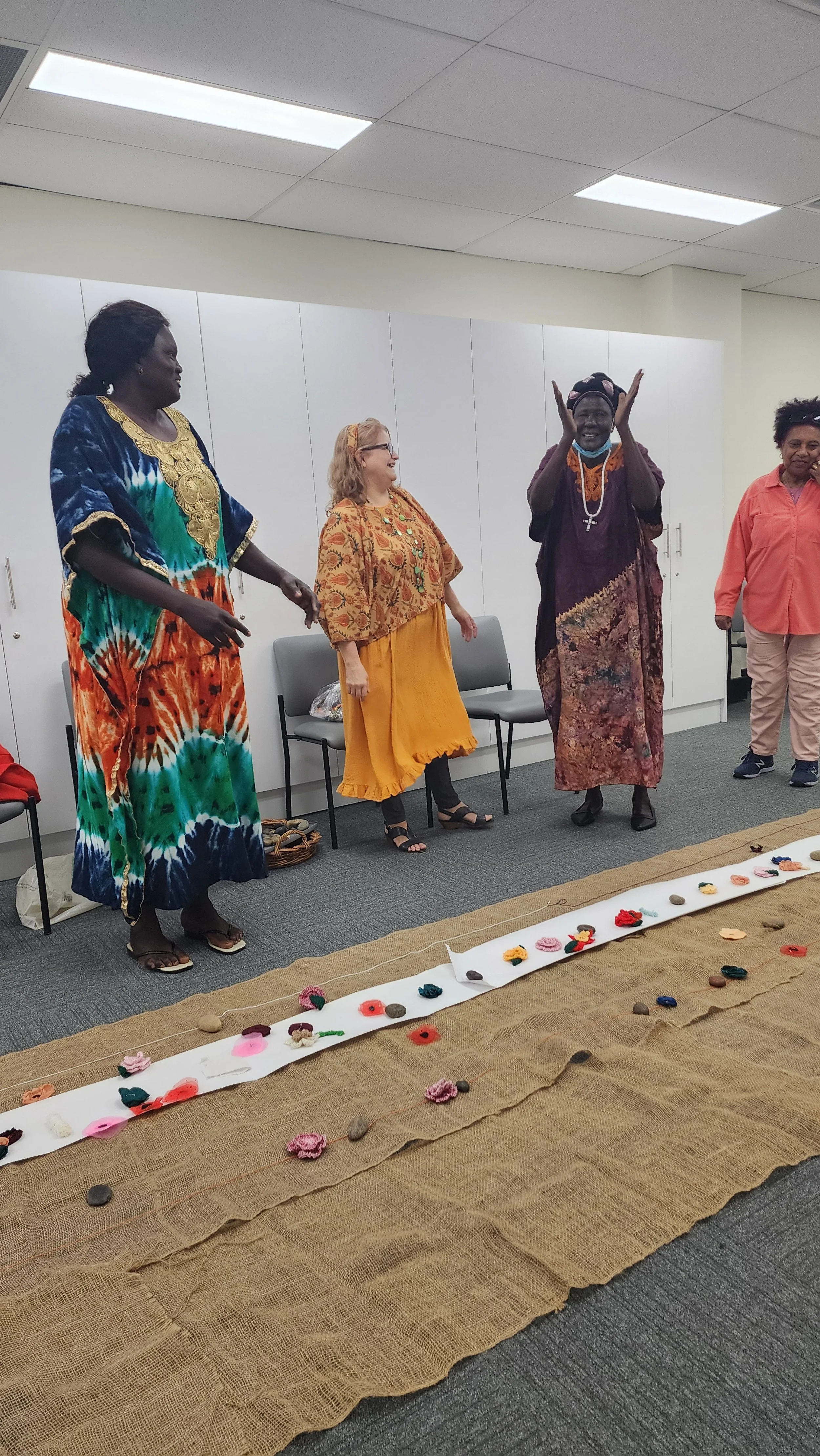 Four women dressed in colorful, traditional African attire standing on a stage with a cloth-covered platform decorated with flowers and stones.