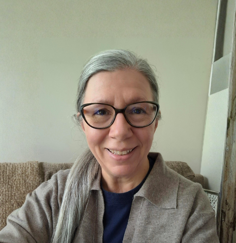 A photo of Jillian Rattray - a woman with gray hair, black glasses, and a beige jacket smiling.