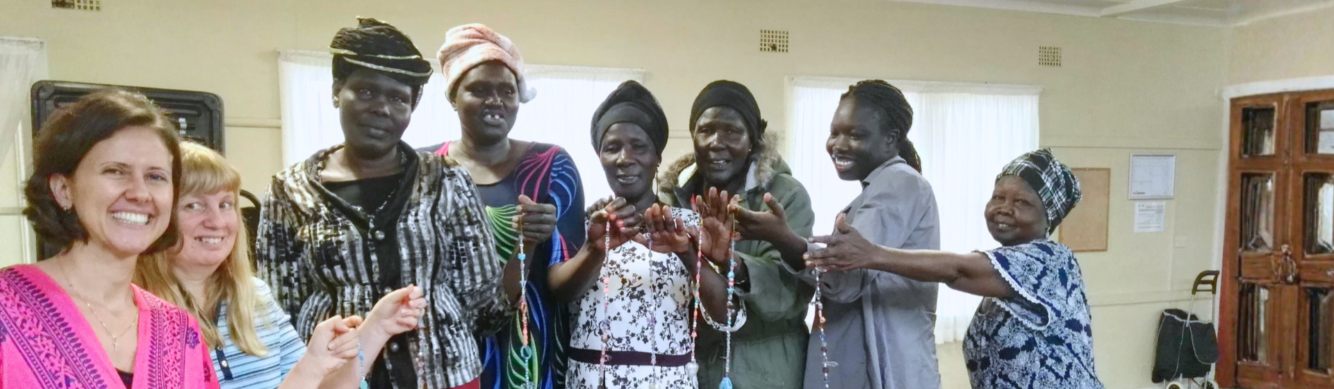 Group of women, some of African descent, holding and displaying jewelry, indoors with light-colored walls and windows