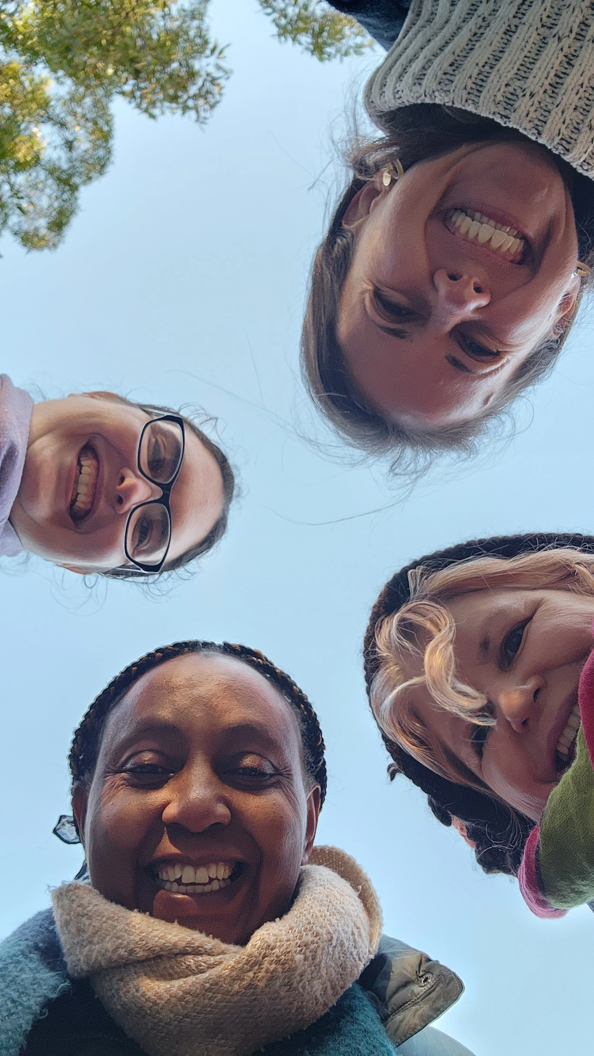 A photo of our four team members, smiling and looking down at the camera outdoors with a blue sky and trees in the background.