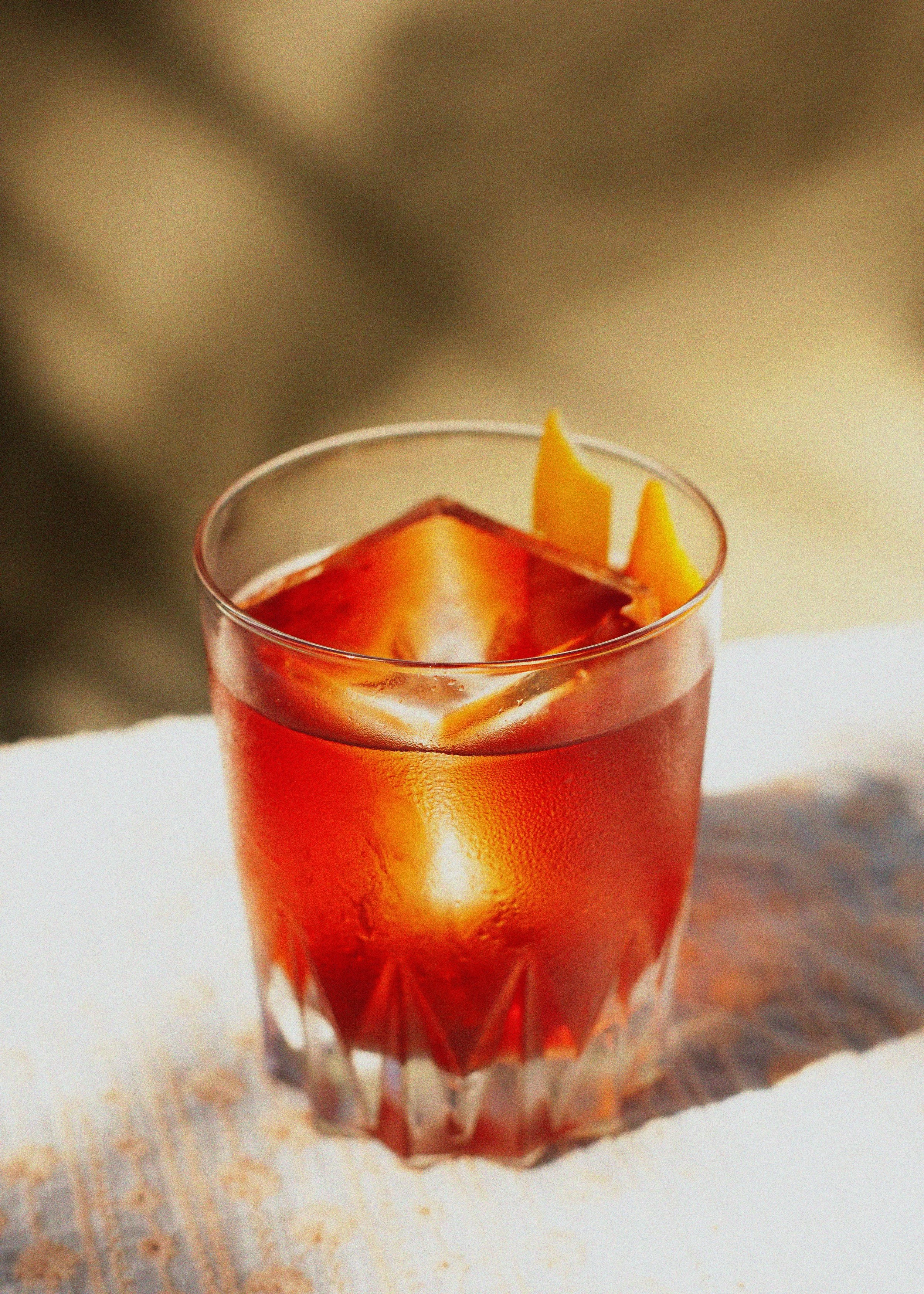 Close-up of an orange cocktail with ice in a rocks glass, garnished with an orange peel twist.