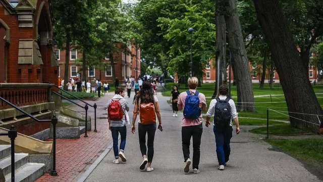 Students walking on a university campus with trees and red-brick buildings