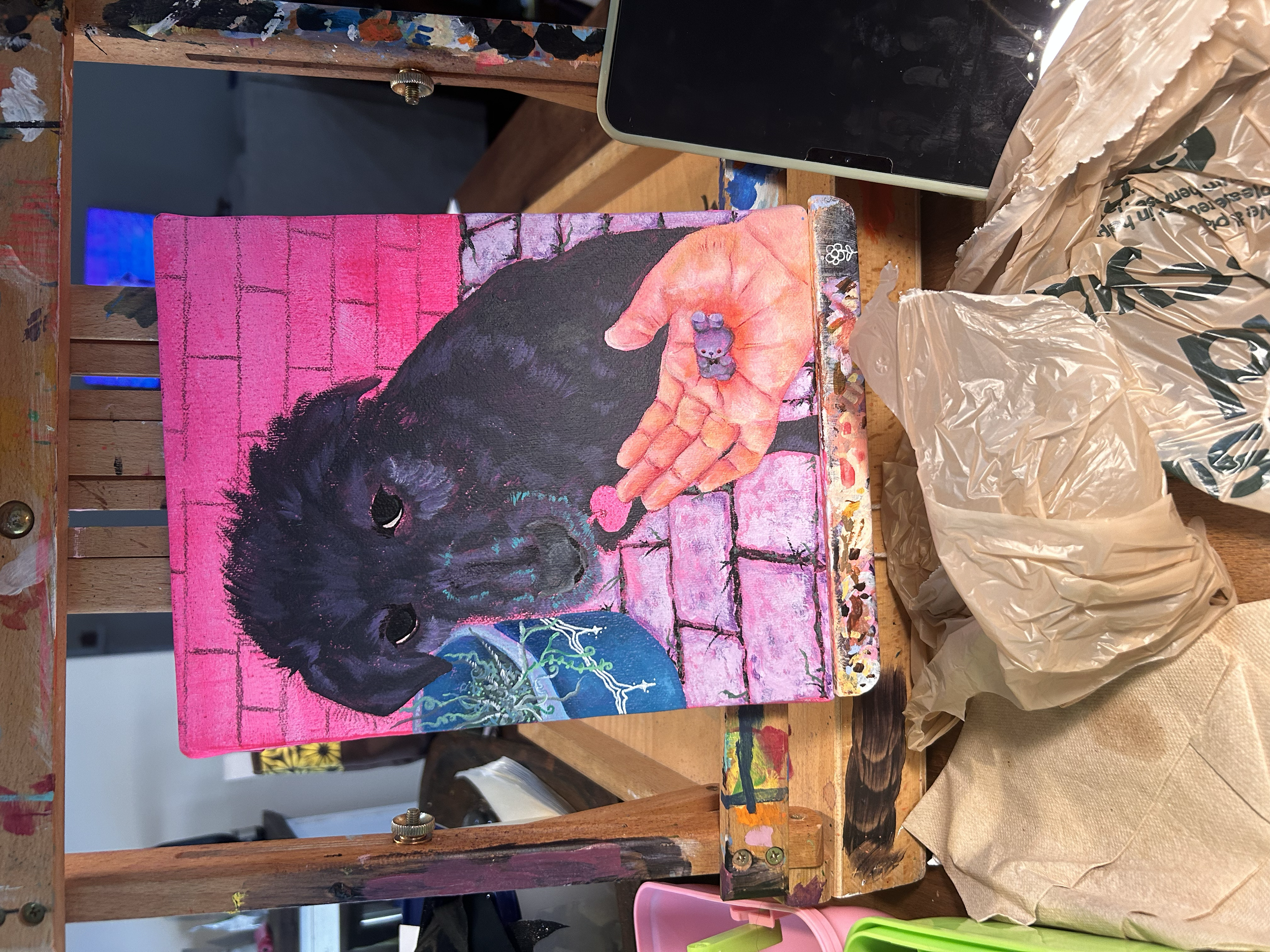 A painting of a black dog with a pink background, holding a small purple stuffed animal in its paw, with a blue ball nearby, on an artist's easel.