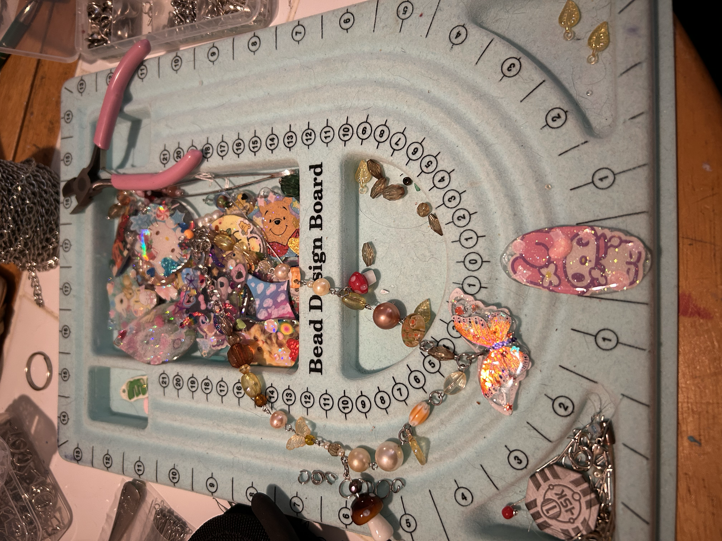 A jewelry-making workspace with a jewelry design board and assorted beads, charms, and jewelry components scattered across the surface.