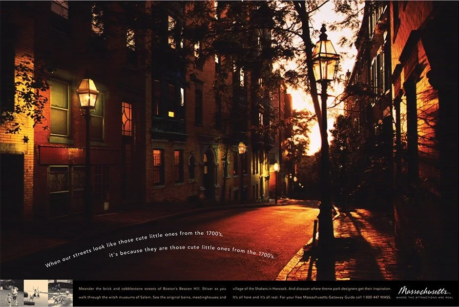 Sunset over historic brick street in Boston with old-fashioned lampposts and trees casting long shadows.