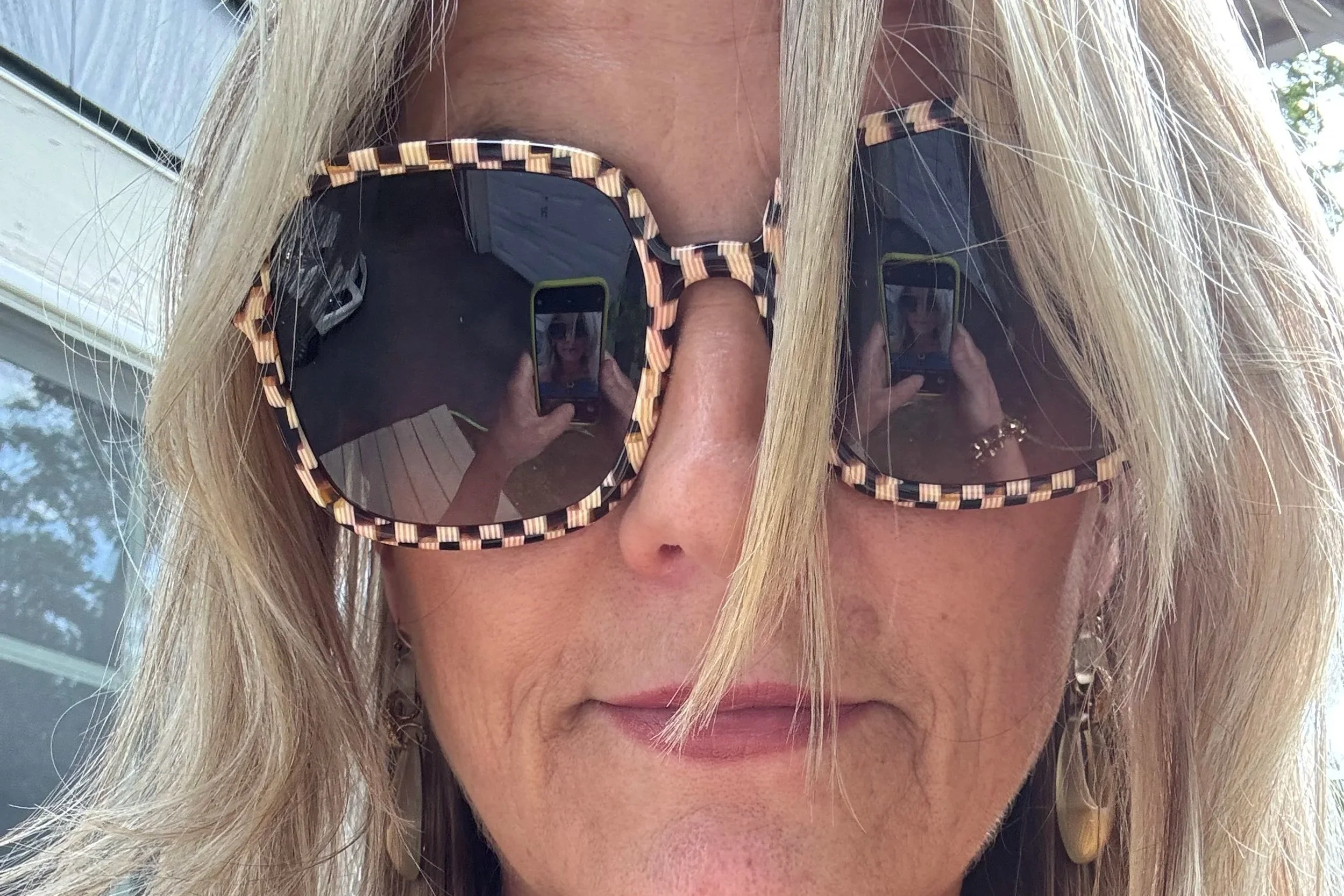 Close-up of a woman wearing large sunglasses with a checkered pattern, with her reflection visible in the lenses.