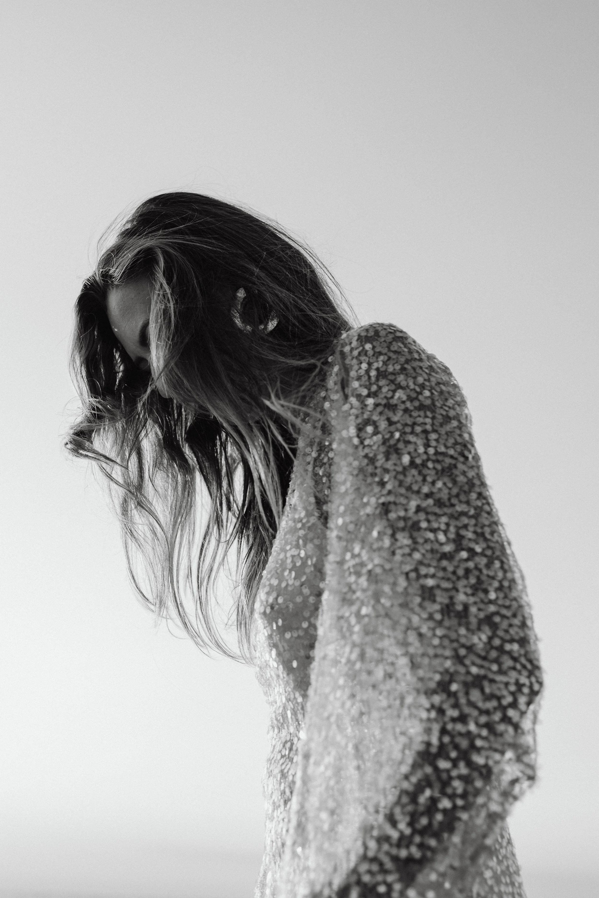Black and white photo of a woman with long, wavy hair, looking down, wearing a textured, sparkly garment.
