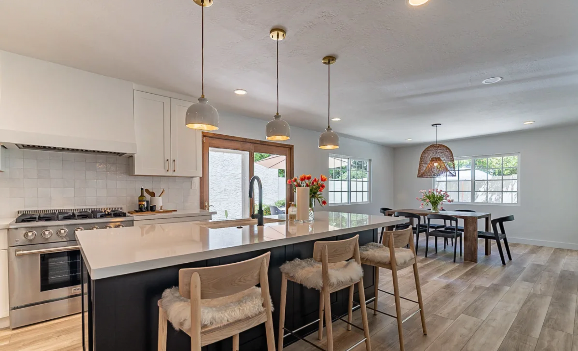 Modern open-concept kitchen and dining area with white cabinets, a large island, light wood floors, and large windows.