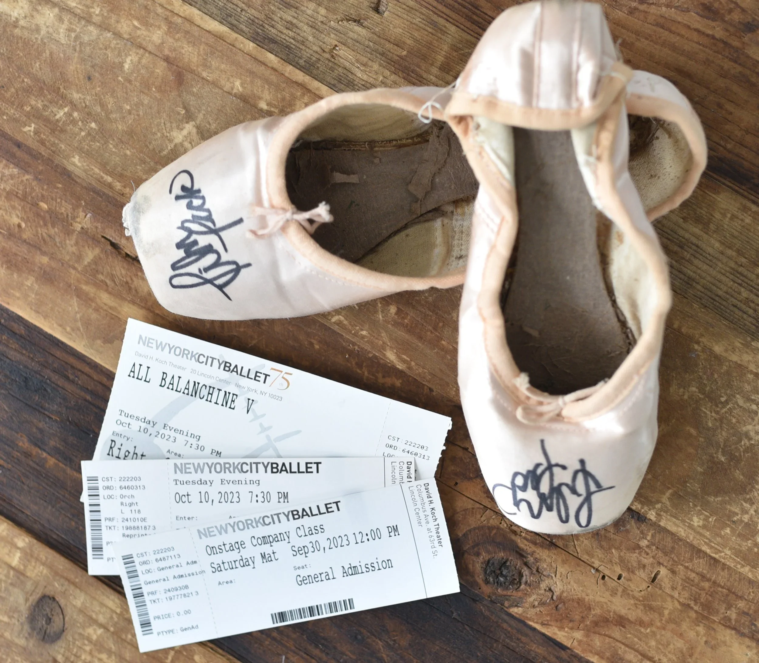 Ballet shoes with autographs and tickets for New York City Ballet on a wooden surface.