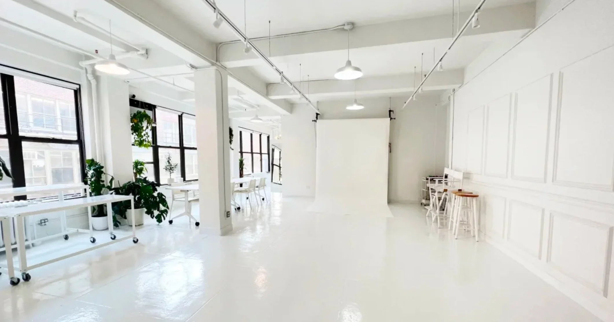 Bright, minimalist, white interior space with large windows, plants, and white furniture.