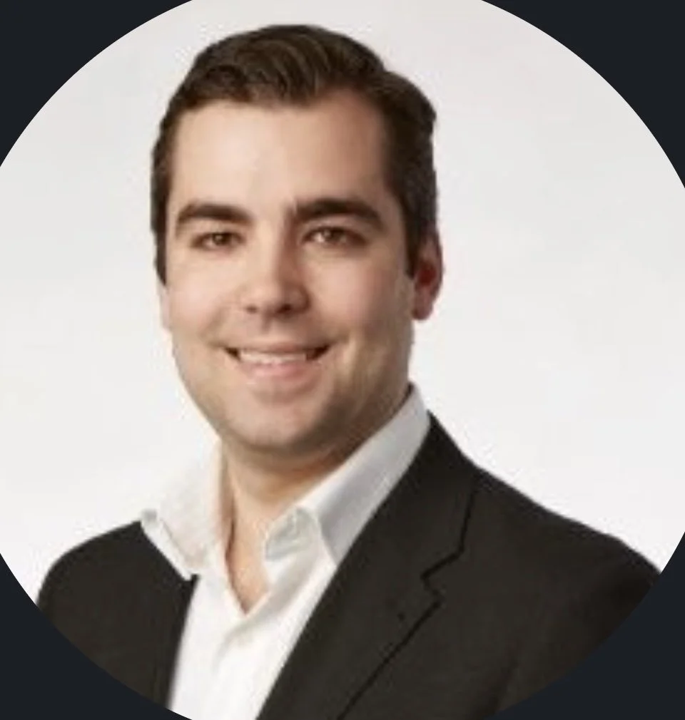 A woman with black shoulder-length hair smiling in front of green leafy plants.
