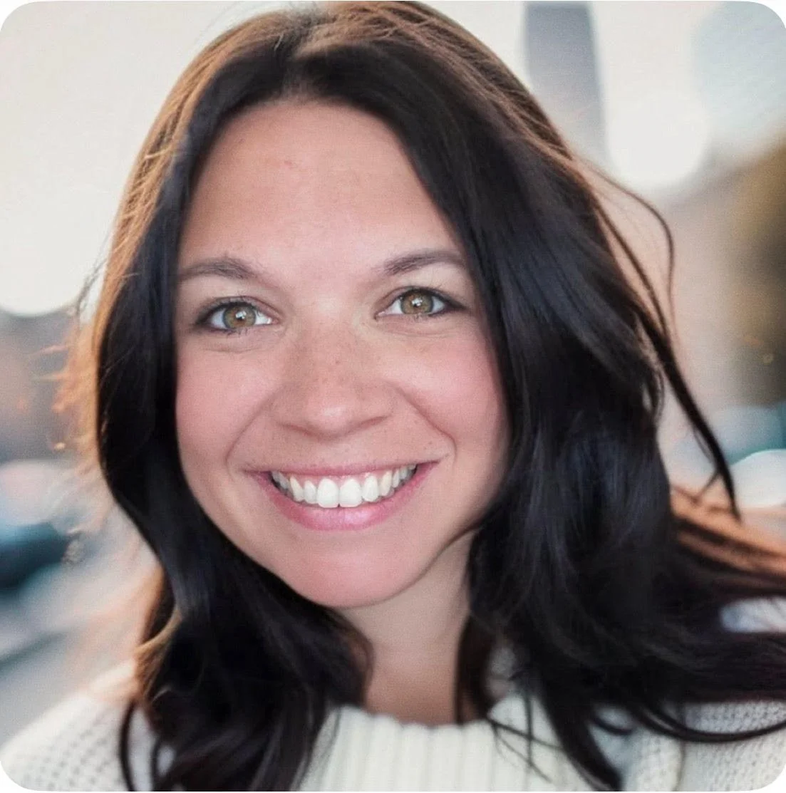 Close-up of a woman with dark hair, smiling, indoors with blurred background.