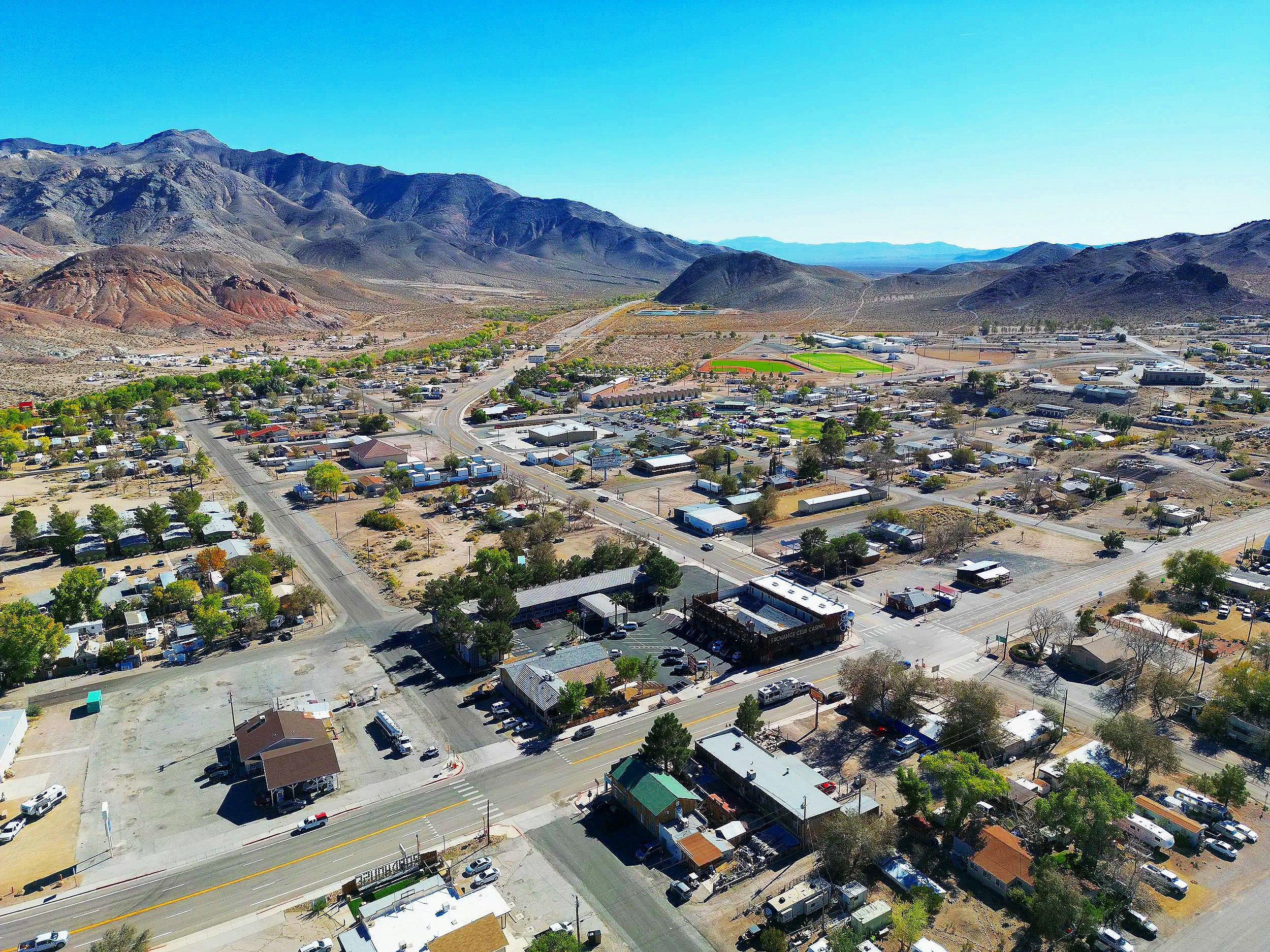 Aerial view of a small town surrounded by mountains, with streets, buildings, and a sports field.