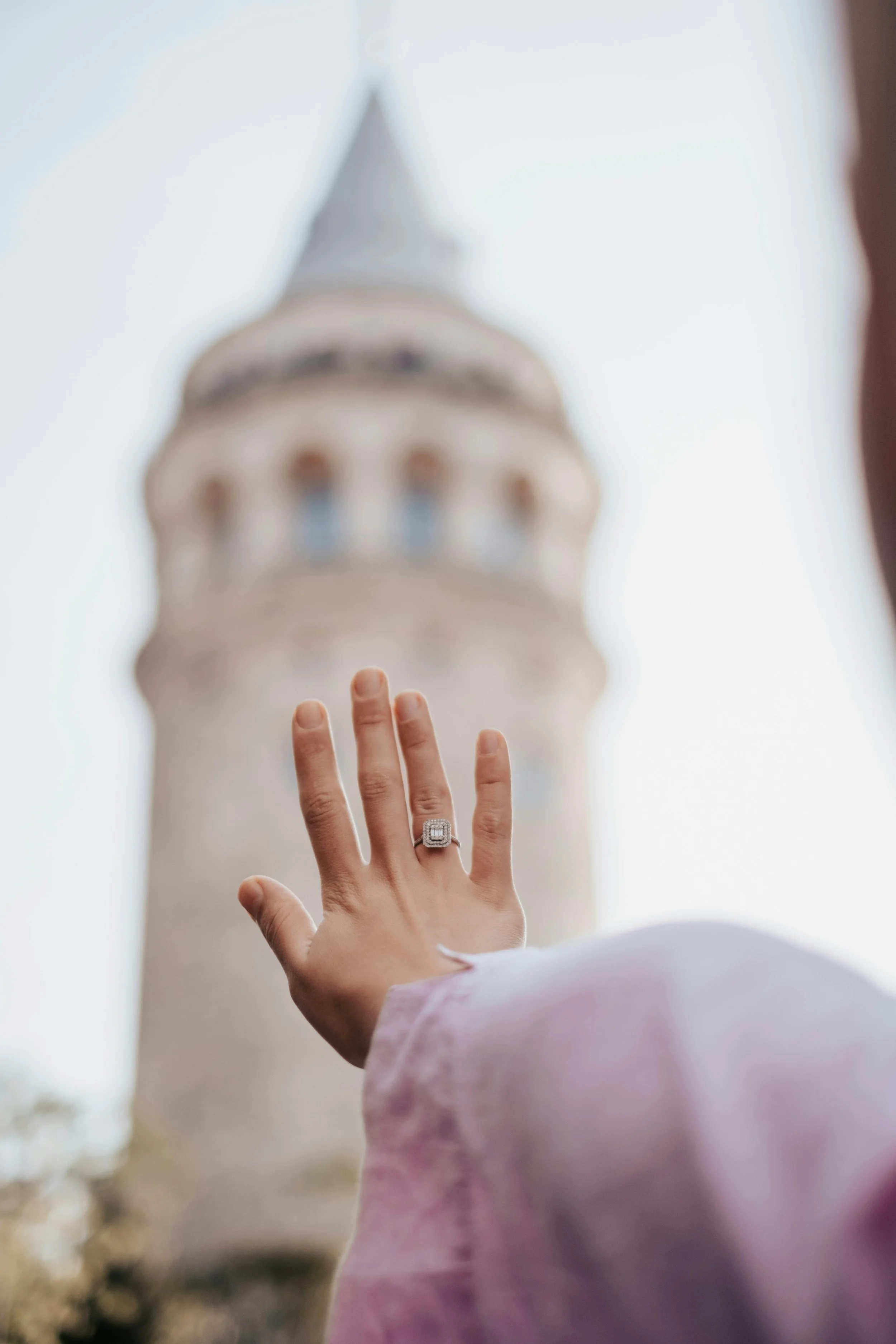 A woman’s hand with a diamond ring reaching out to touch the base of a church tower, with the tower blurry in the background.