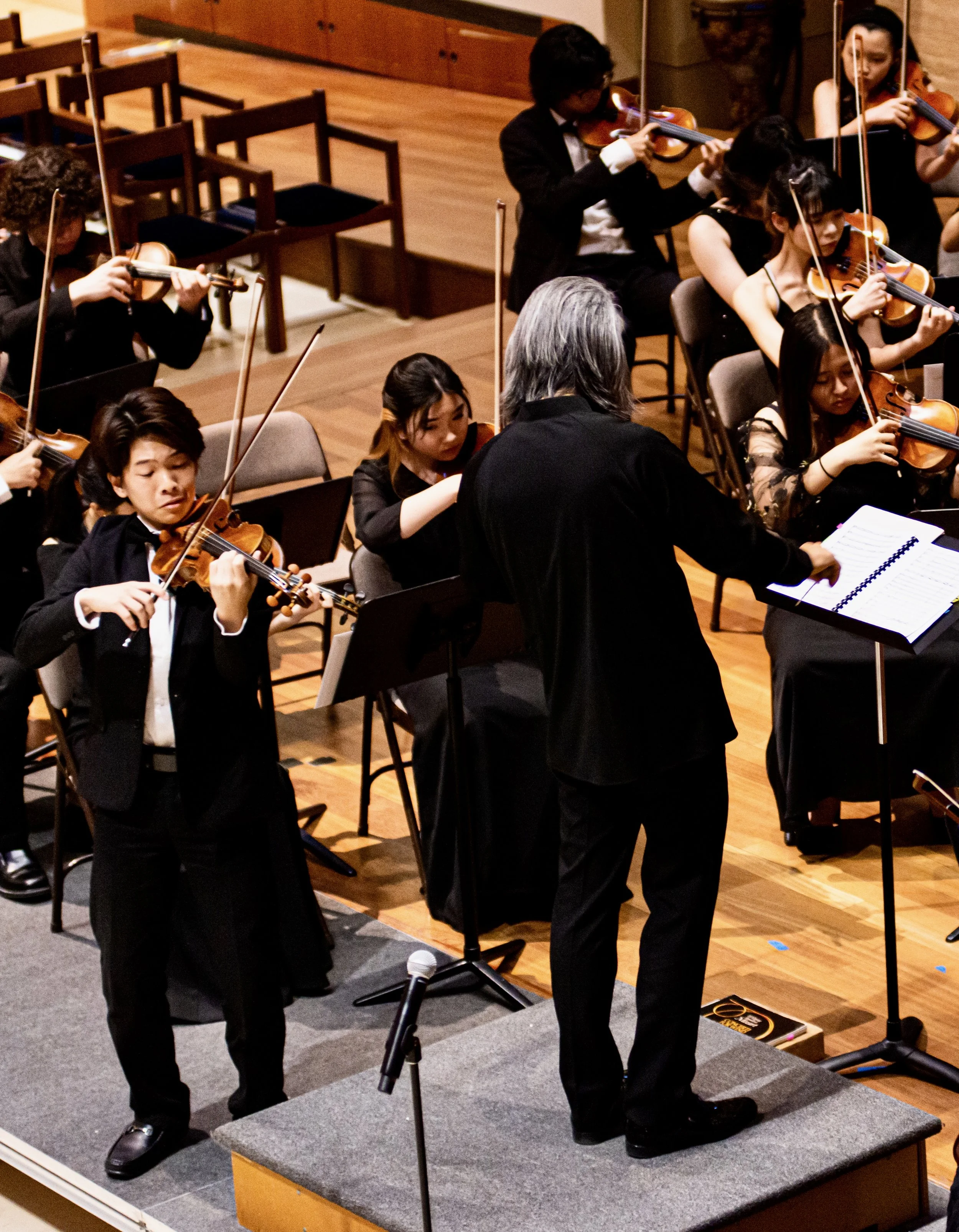 Orchestra conductor leading young musicians playing violins during a performance.