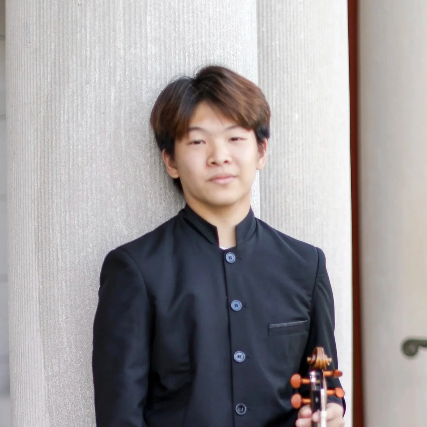 Young man standing against a textured wall, holding a violin.