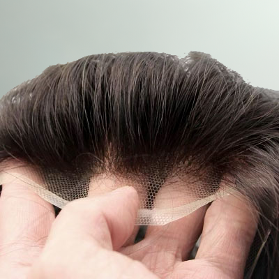 A barber is applying a hair system to a client's scalp.