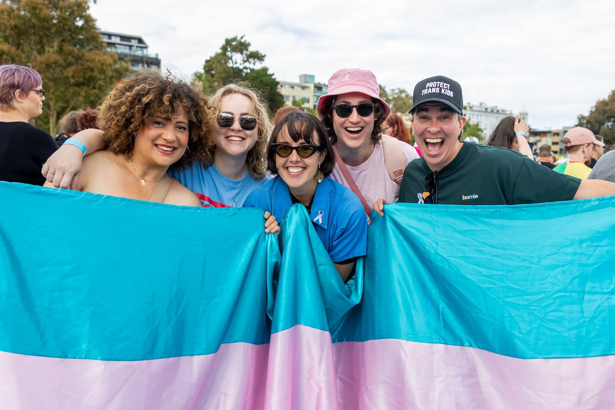 A group of smiling people holding a trans flag at a march