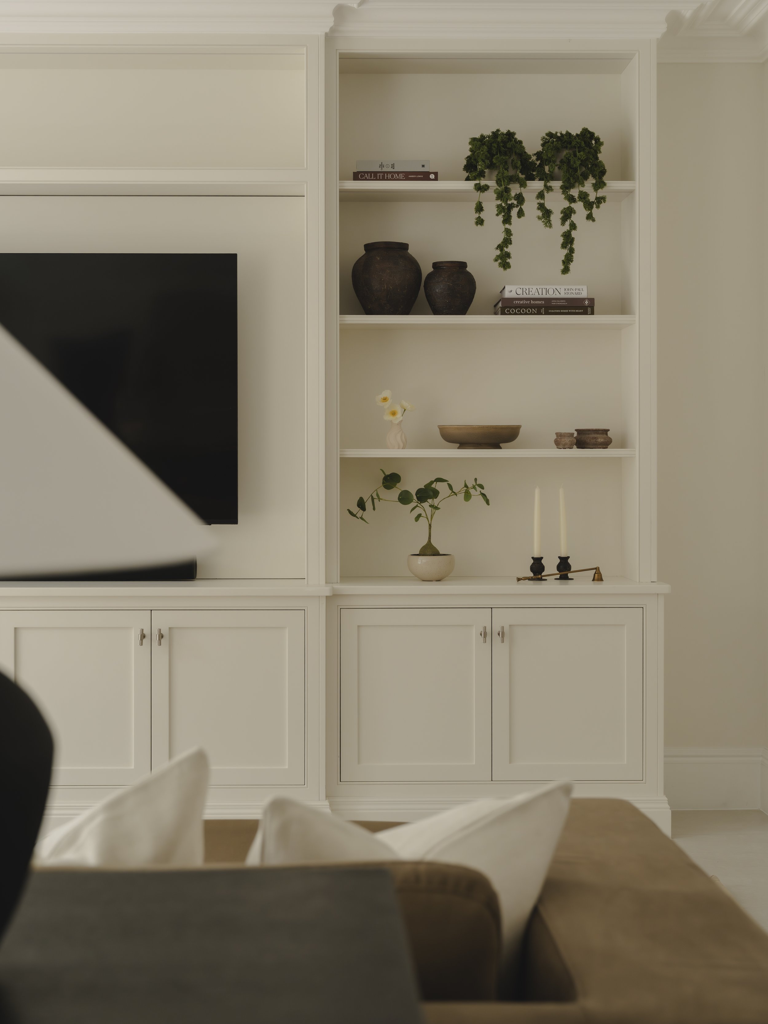 Living room with white built-in shelves displaying decorative vases, plants, candles, and books.