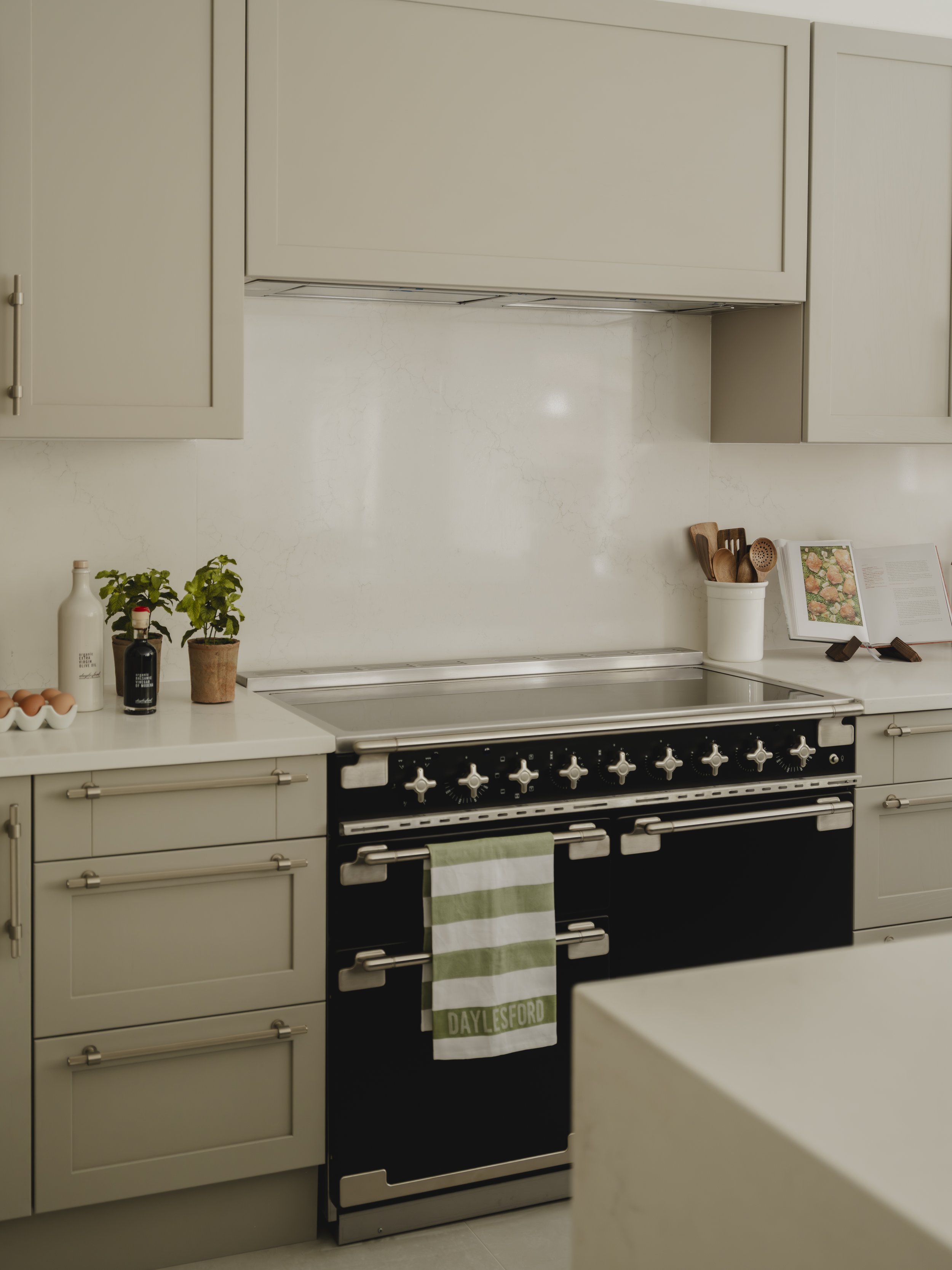 Kitchen with beige cabinets, black stove, countertop with eggs, potted plant, book, and utensils in a container.