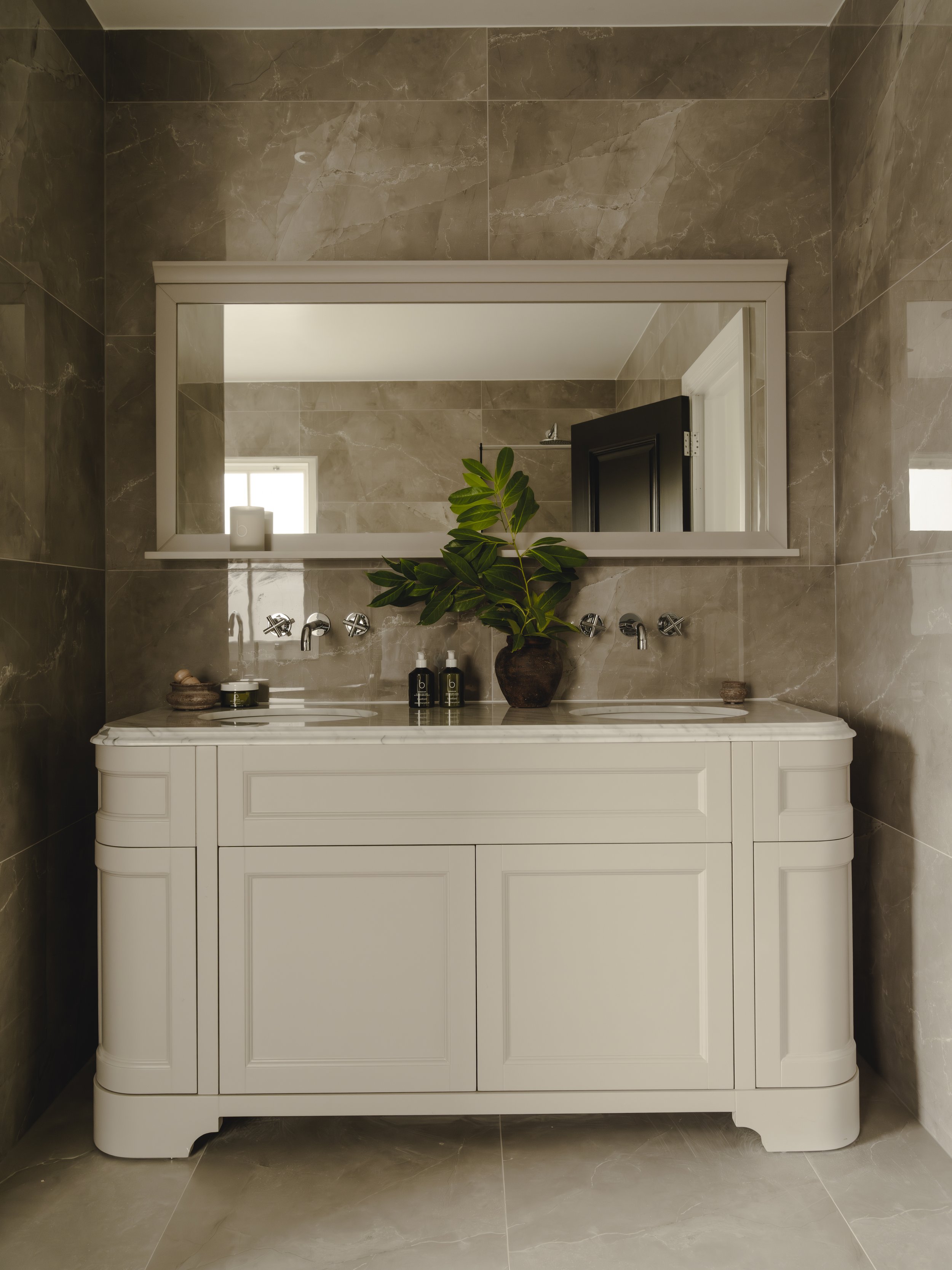 Bathroom with white vanity, large mirror, green plant, beige tiled walls and floor.