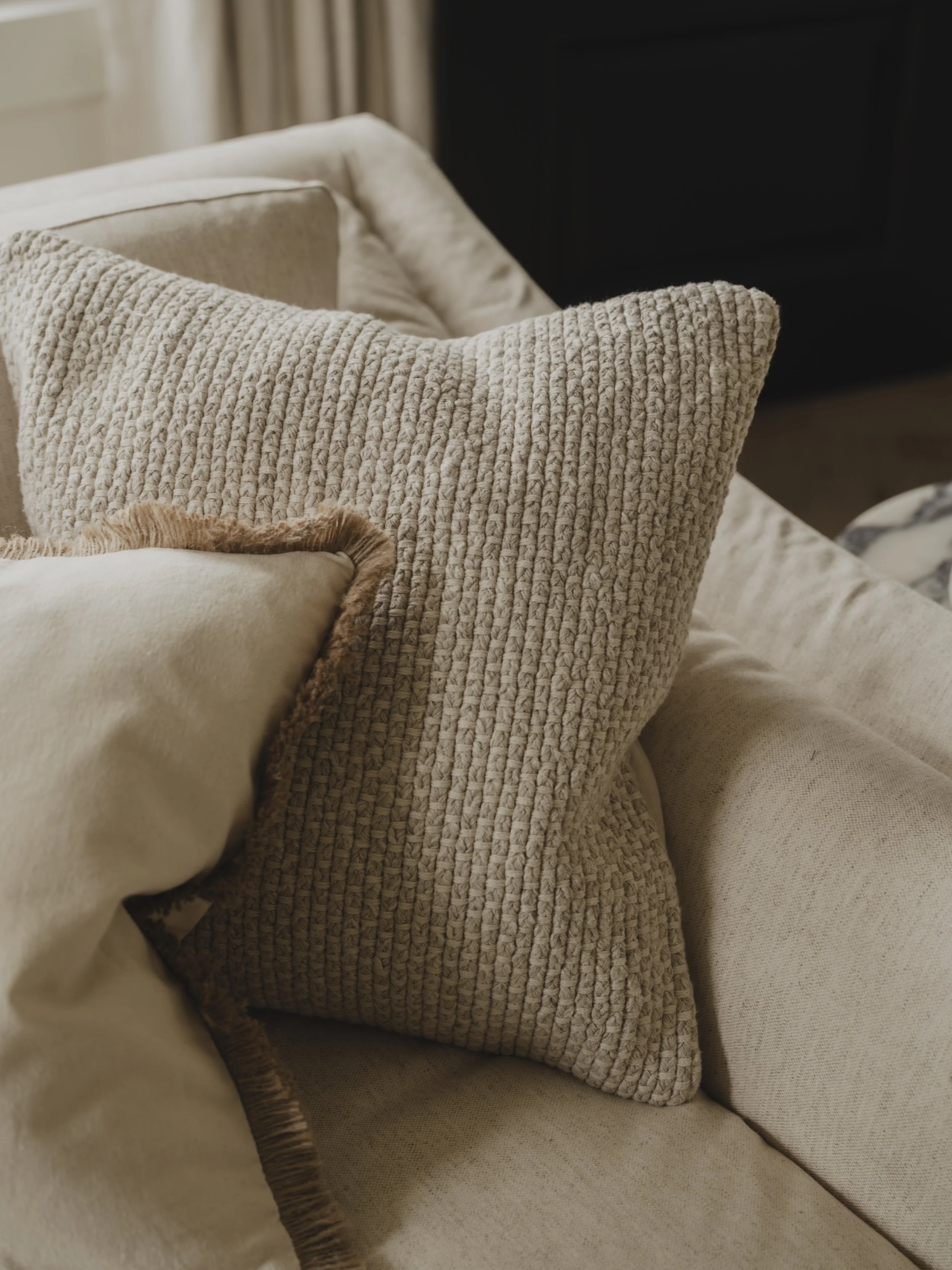 Close-up of several beige and cream-colored decorative throw pillows on a beige sofa in a living room.