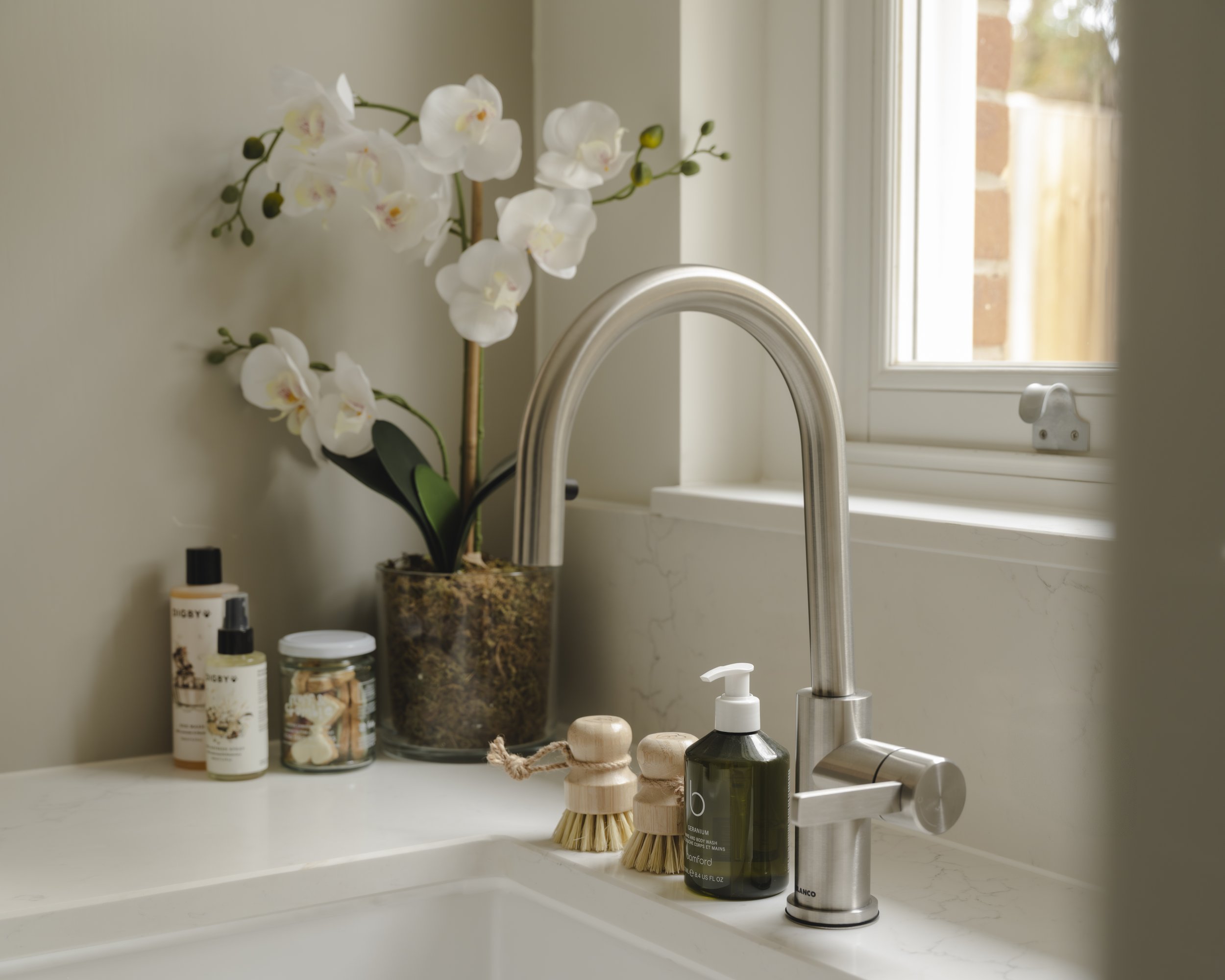 Bathroom sink with orchid plant, soap dispenser, brushes, and lotion bottles near window