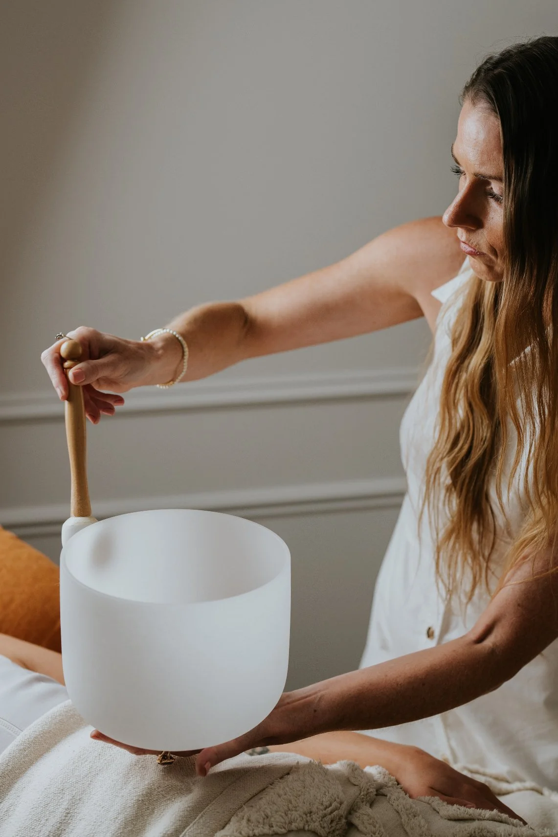 A woman using a singing bowl with a mallet, performing a sound healing session, in a calm and serene setting.