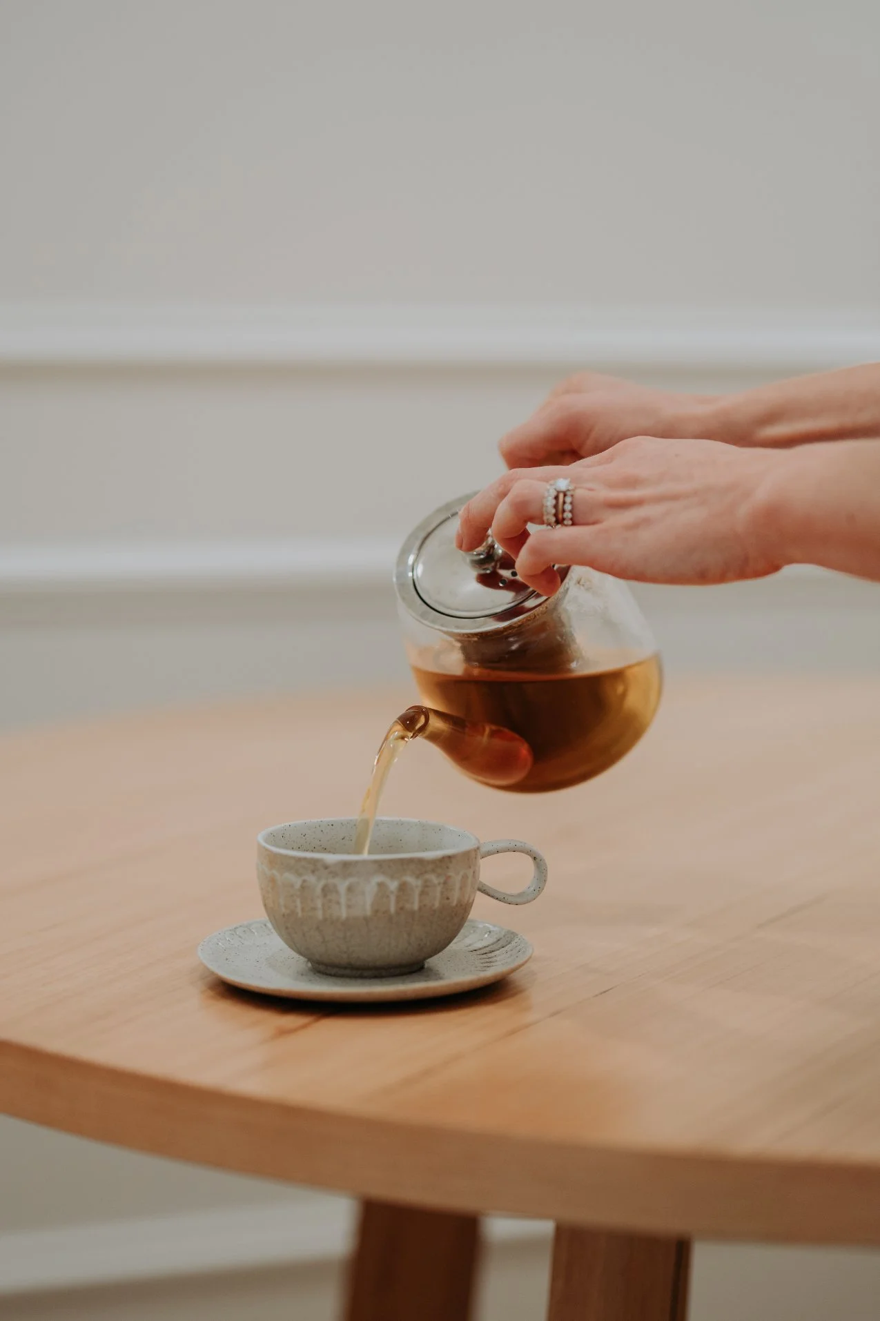 Hand pouring tea into a ceramic cup on a wooden table