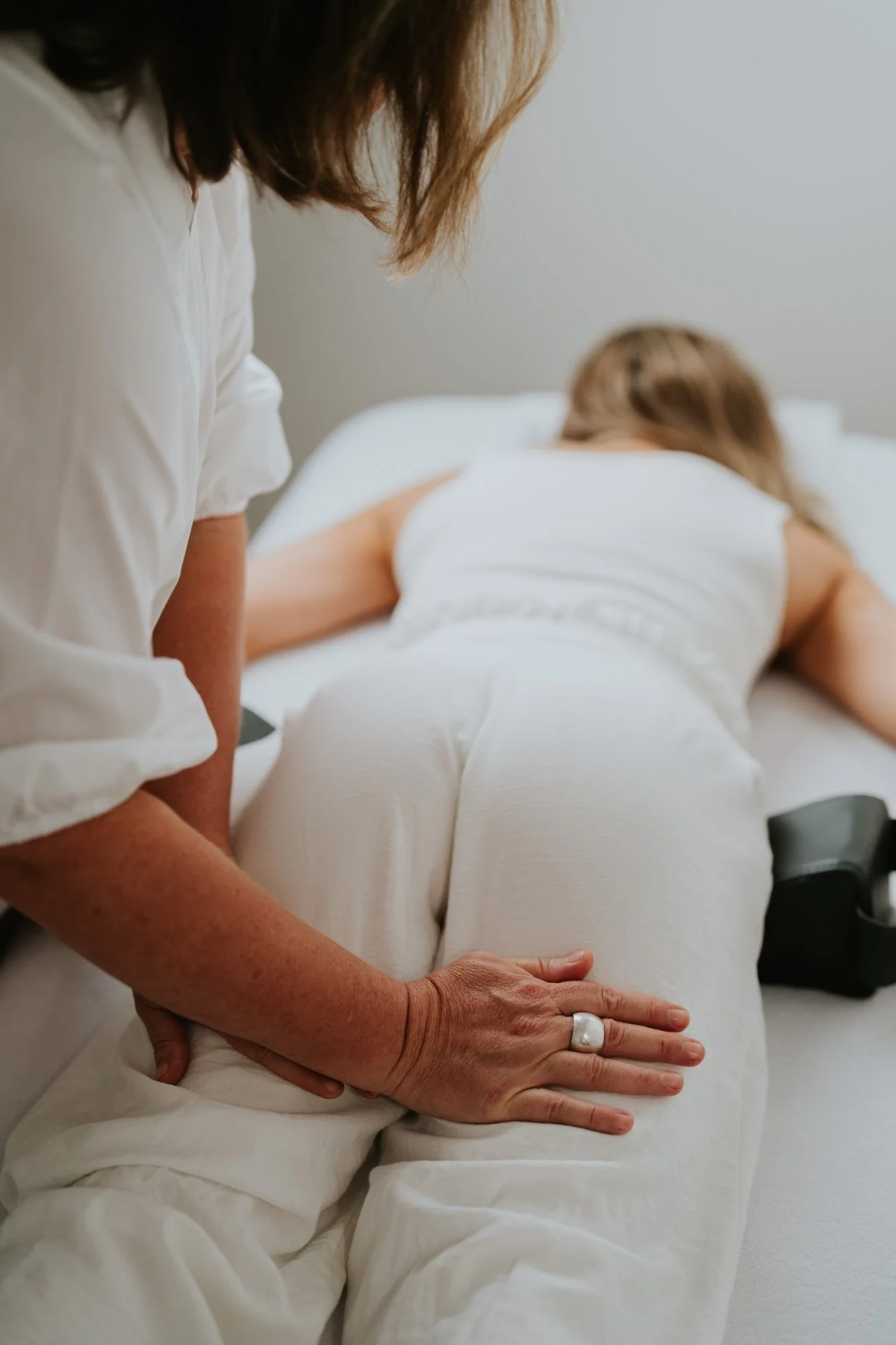 A person lying face down on a bed receiving a massage from another person.