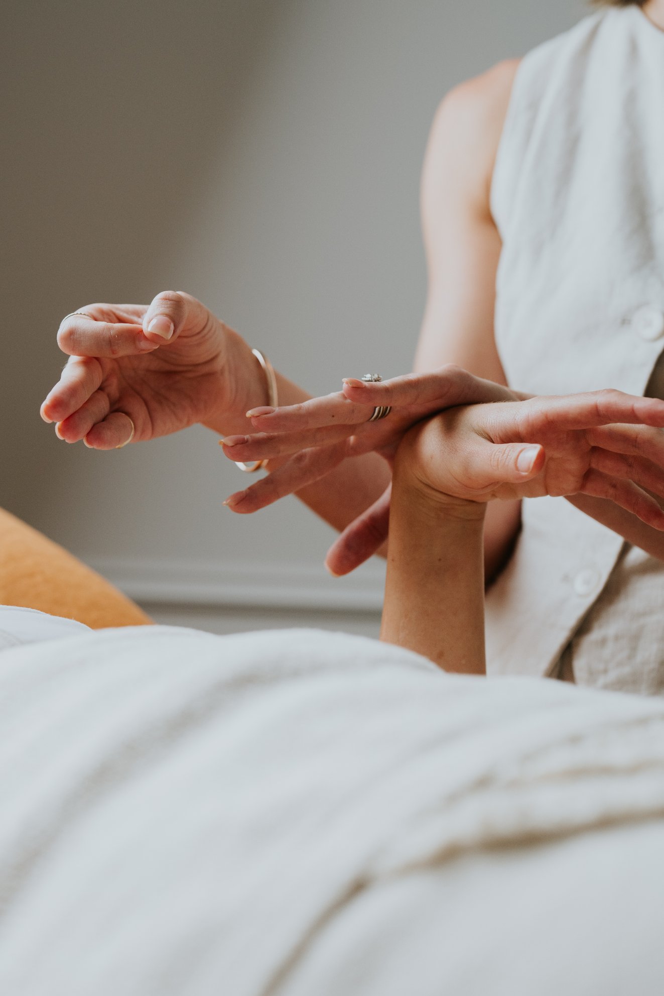 Close-up of a woman holding another person's hand, showing a wedding ring, with a neutral background.