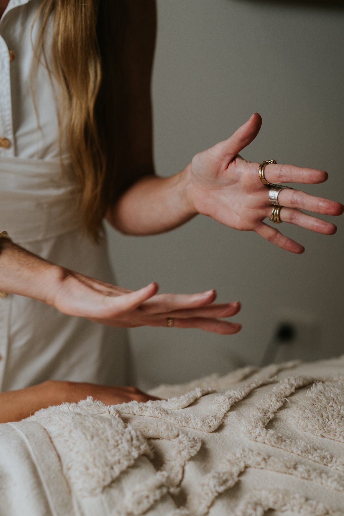 Person with long hair wearing rings and jewelry gesturing with hands above a soft, plush blanket or towel.