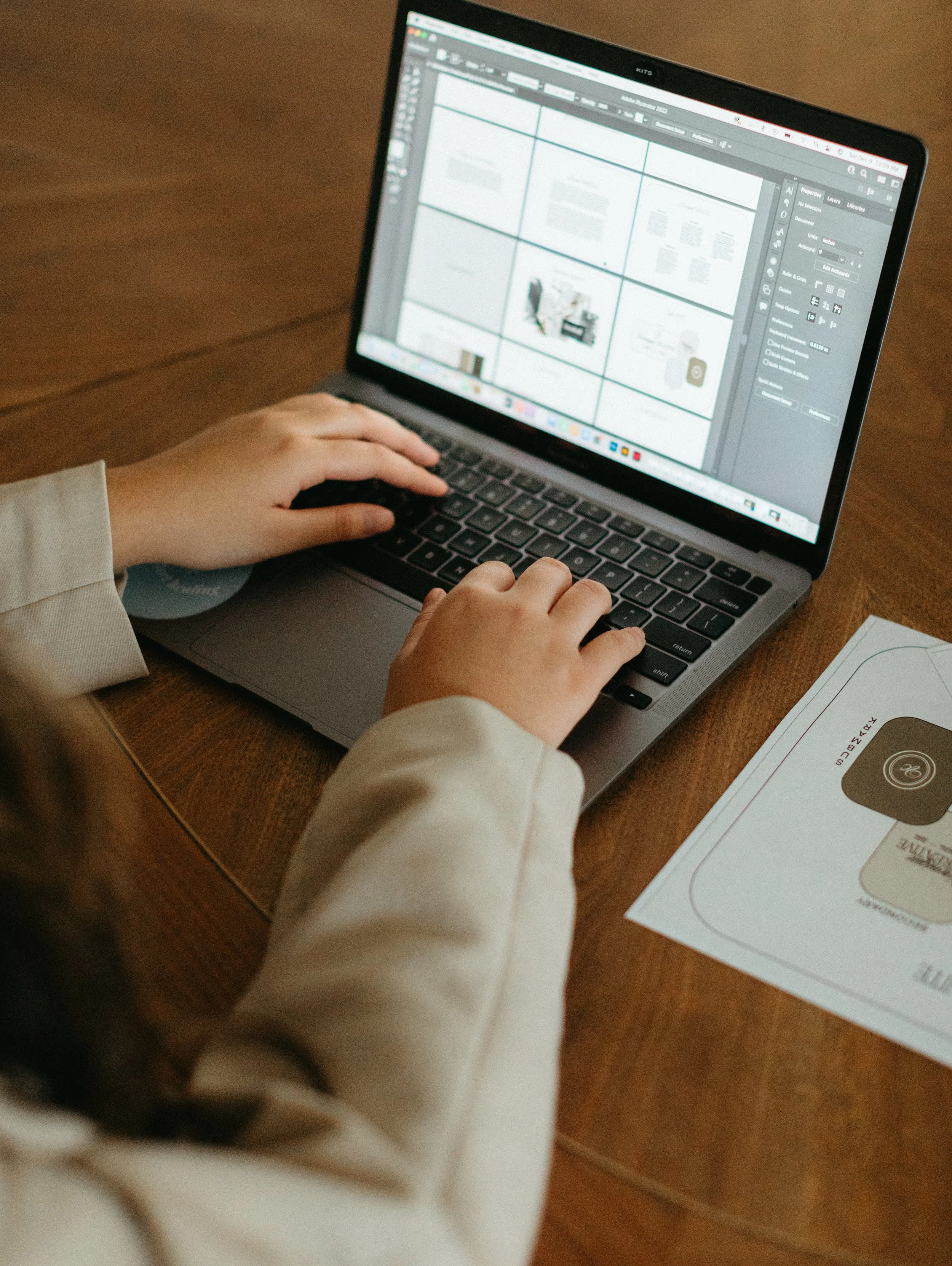 Child working on a laptop at a wooden table with design software open on screen and printed design plans nearby.