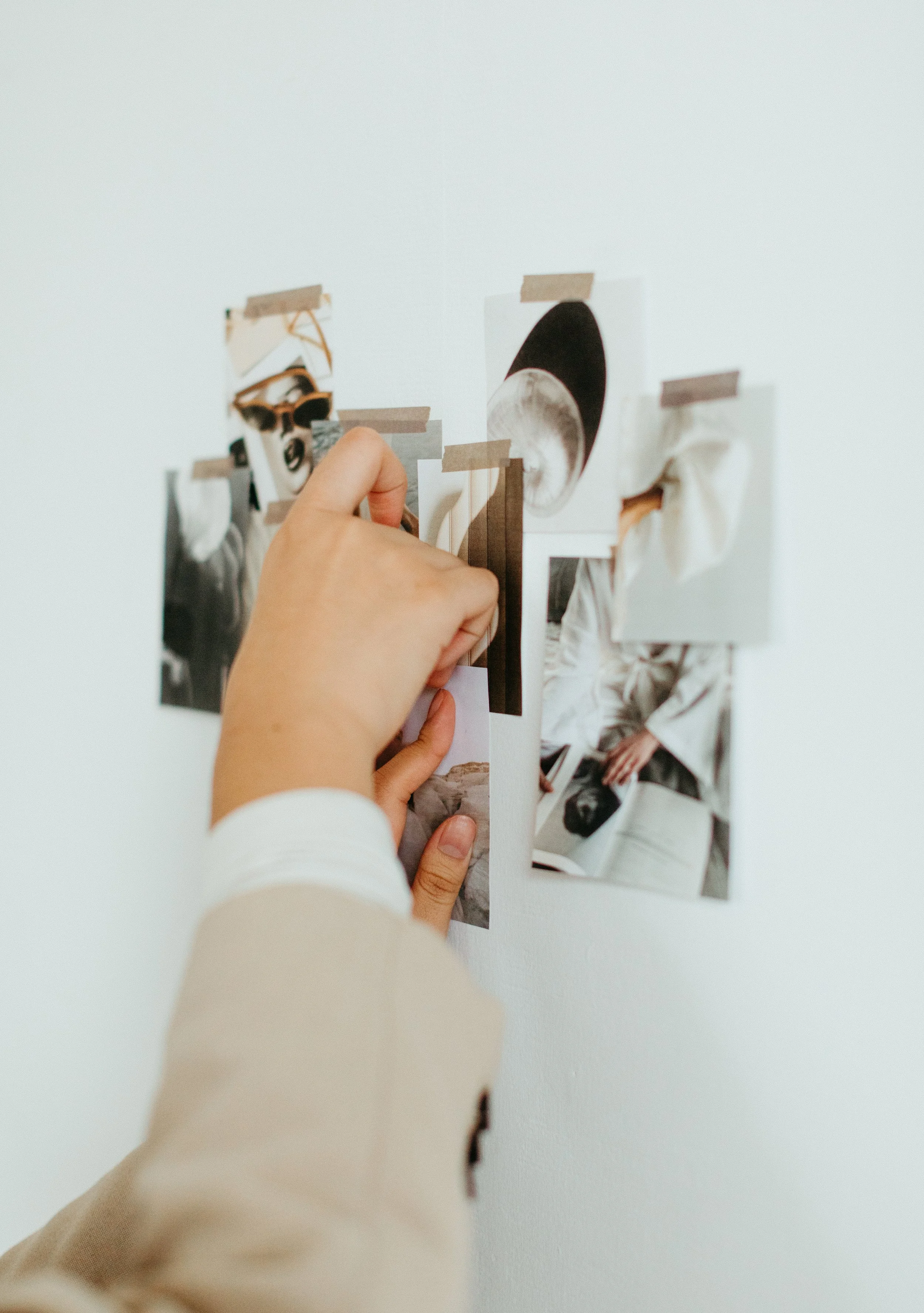 Person arranging photographs on a white wall with tape.