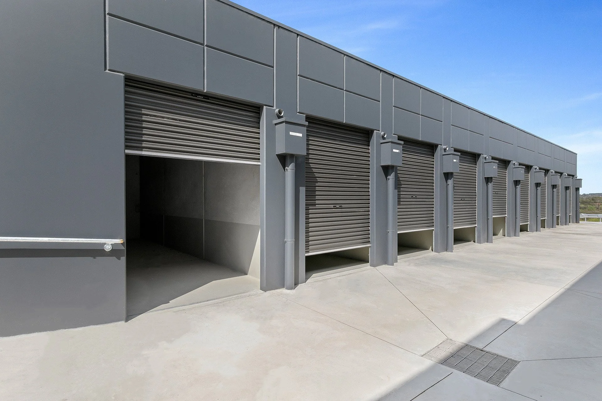 A modern industrial building with closed metal roll-up doors on a concrete surface under a blue sky.