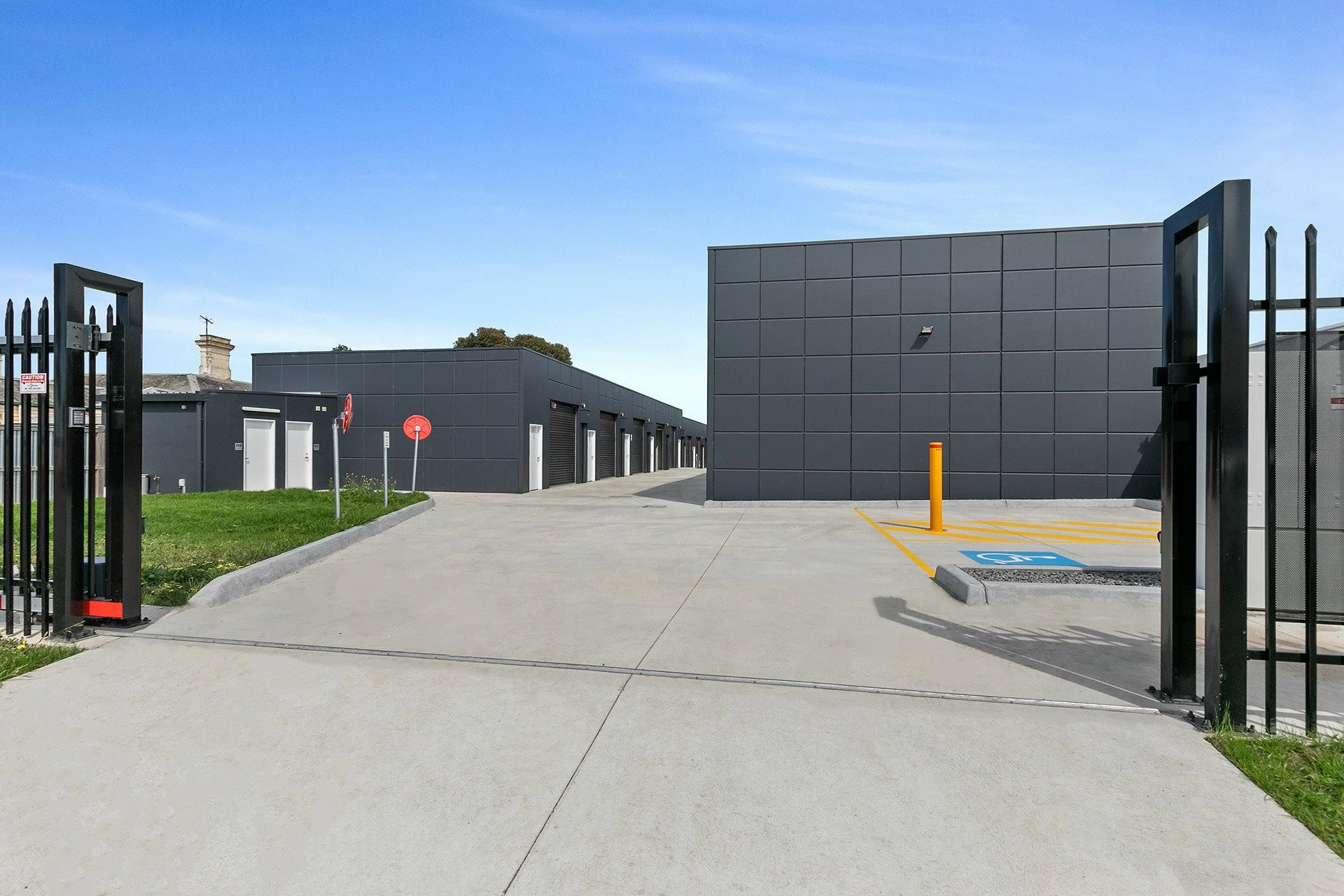Industrial storage units with gates, parking space, and a handicapped parking spot, under a clear blue sky.