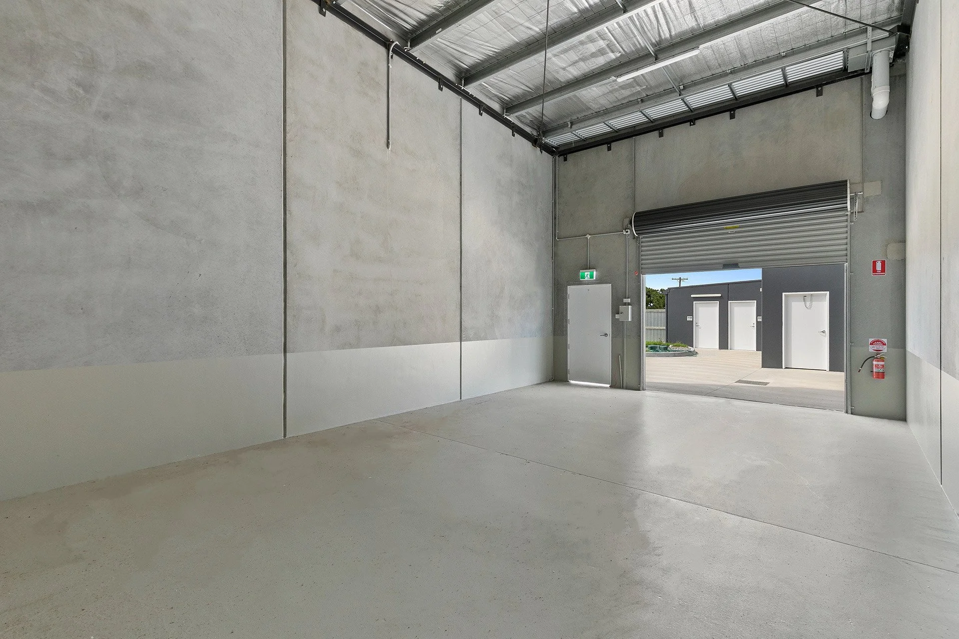 Empty industrial loading dock with open roll-up door, concrete floor and walls, and a fire extinguisher on the right wall.