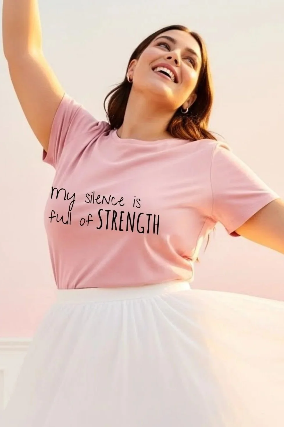A woman smiling with her arm raised, wearing a pink t-shirt with the words 'My silence is full of strength' printed on it, and a white skirt.