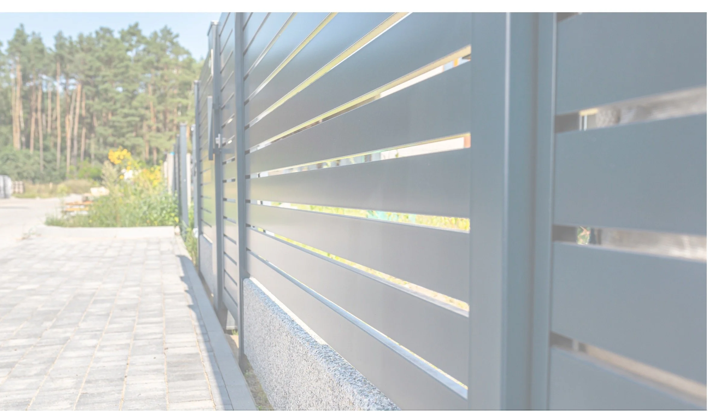 金属のフェンスと石の歩道と植物と木々が写っている風景