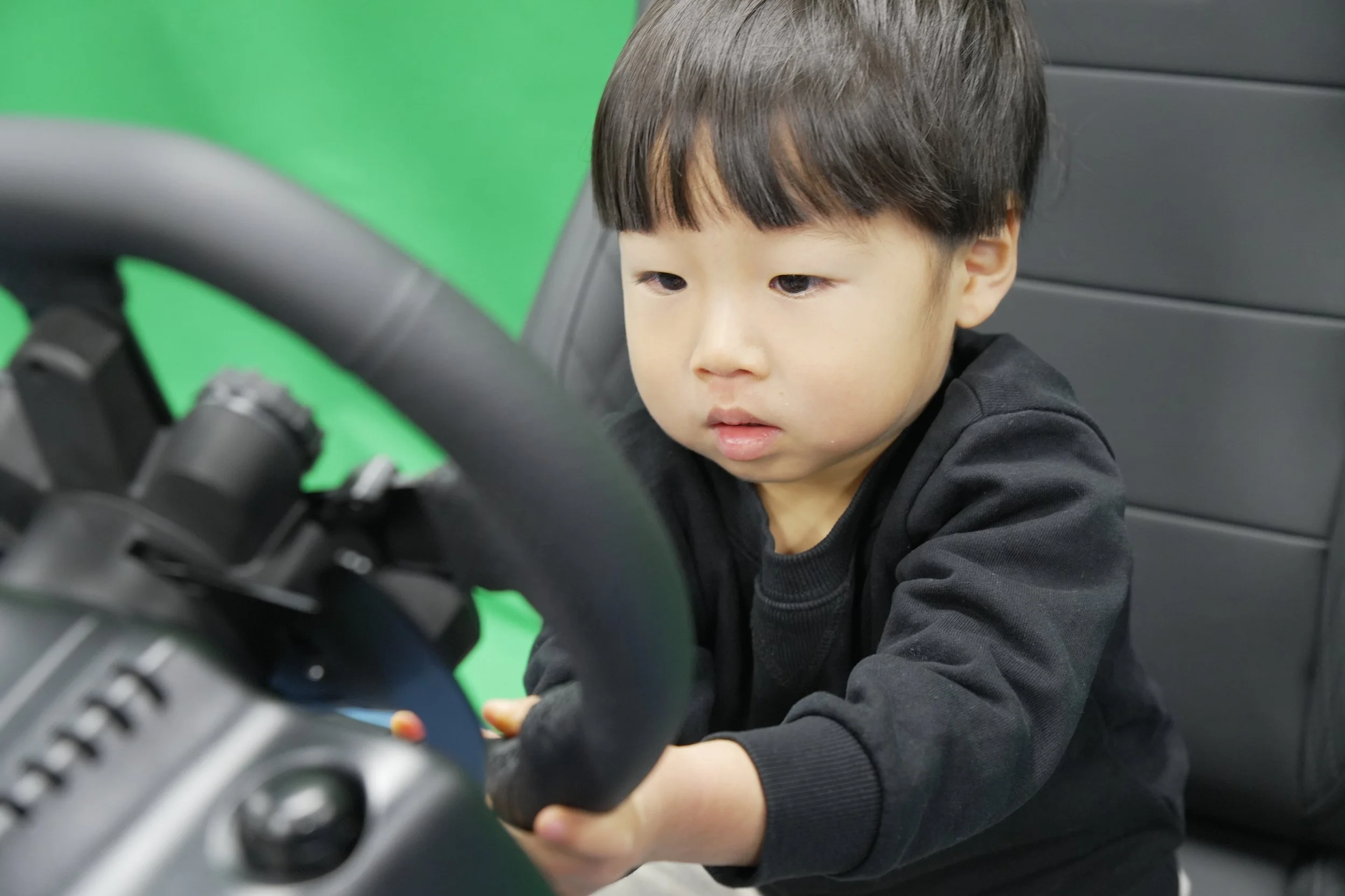 子供が車の運転席に座ってハンドルを握っている写真